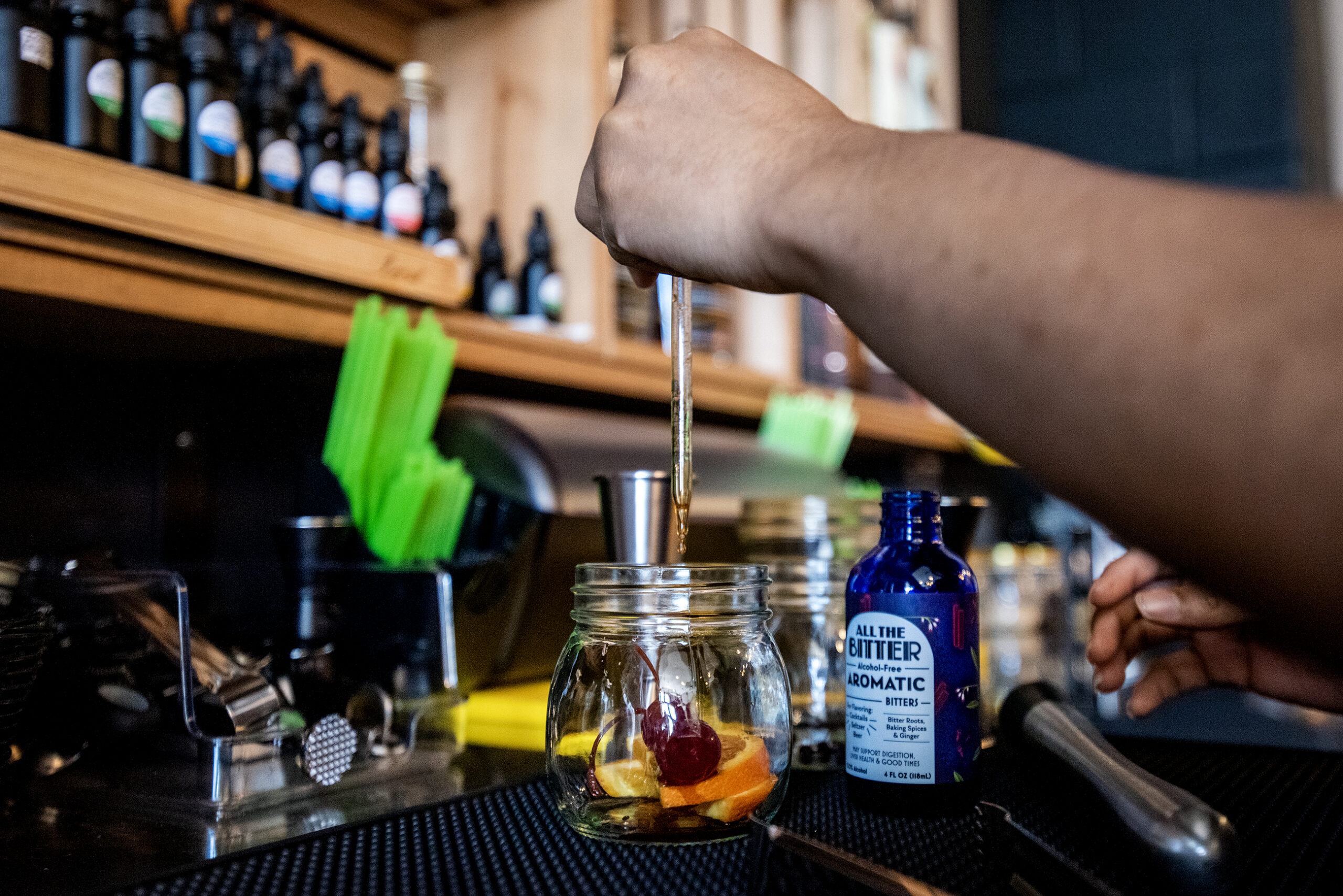 Oranges and cherries are placed in a small jar. An employee uses a dropper to add to the drink.