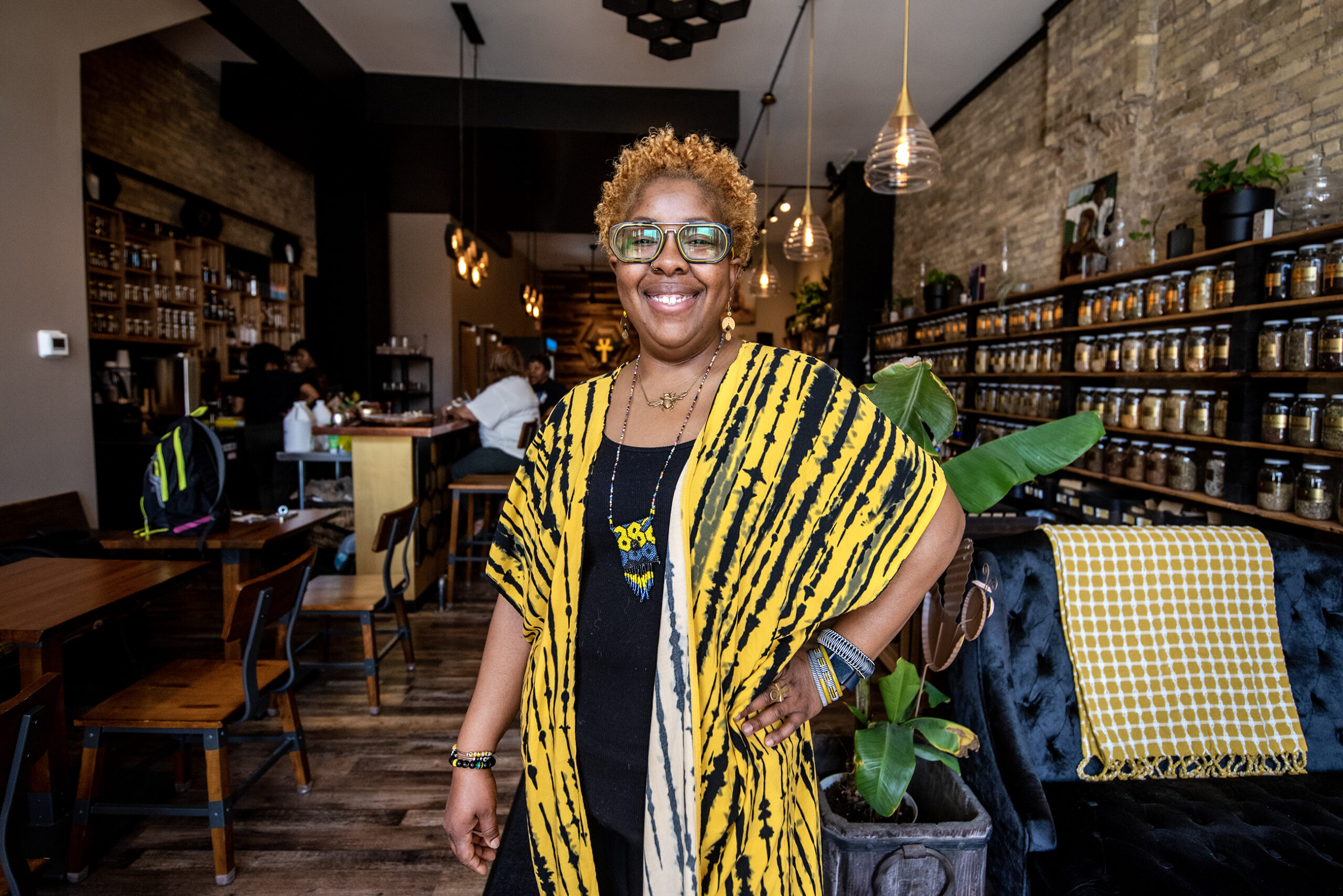 A woman in a yellow outfit smiles inside her bee-themed business.