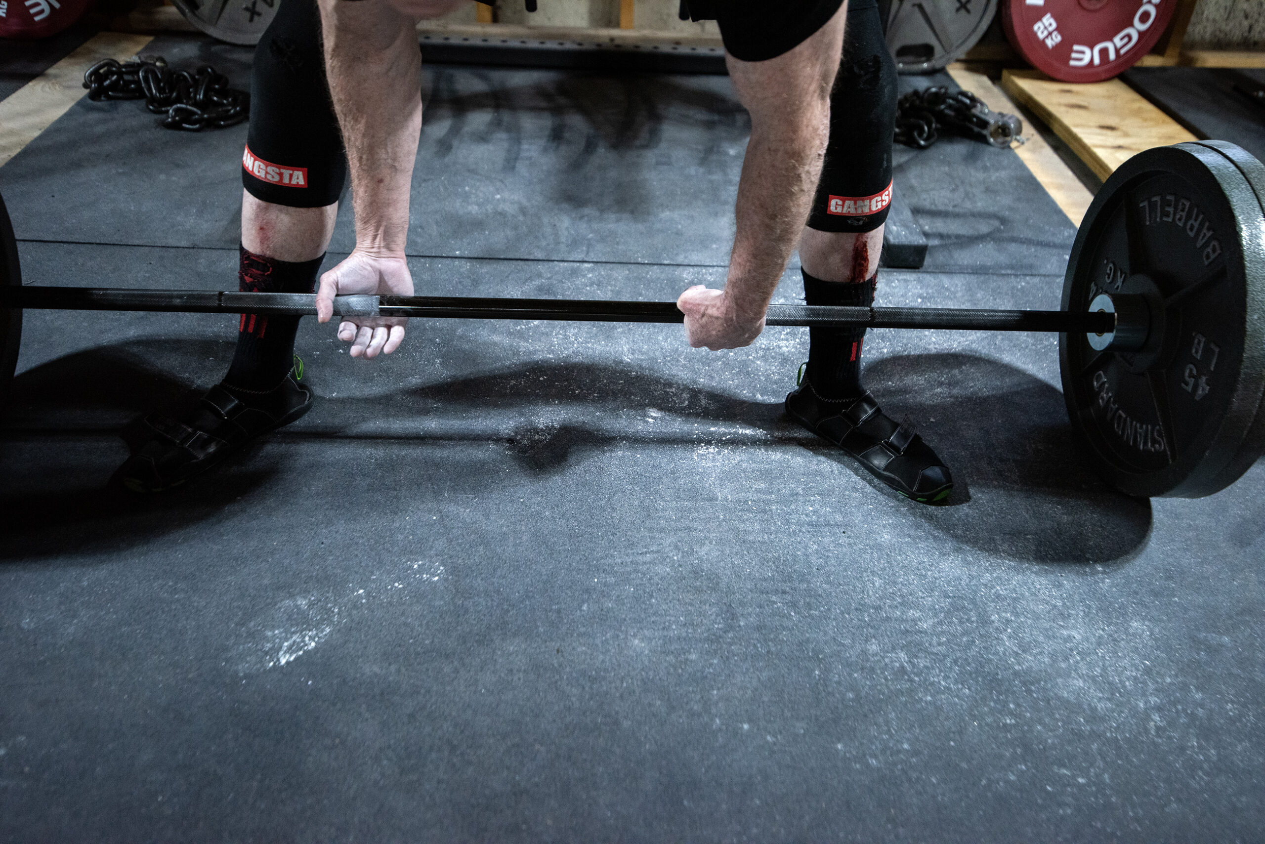 Michael Love's hands are white with chalk as he grabs the bar. Red blood can be seen on the front of his shins.