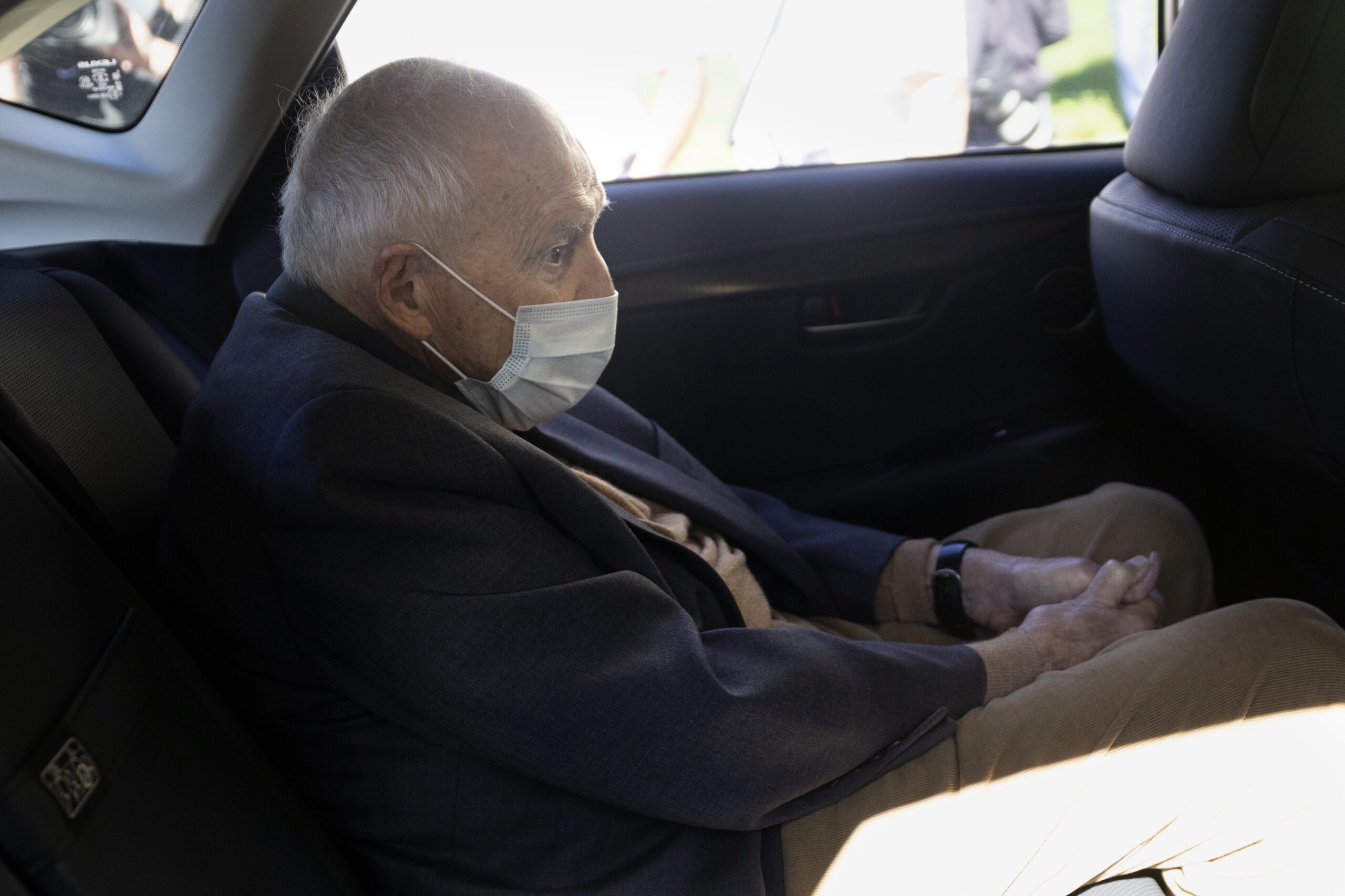 Theodore McCarrick wears a facemask sitting in the back of a car