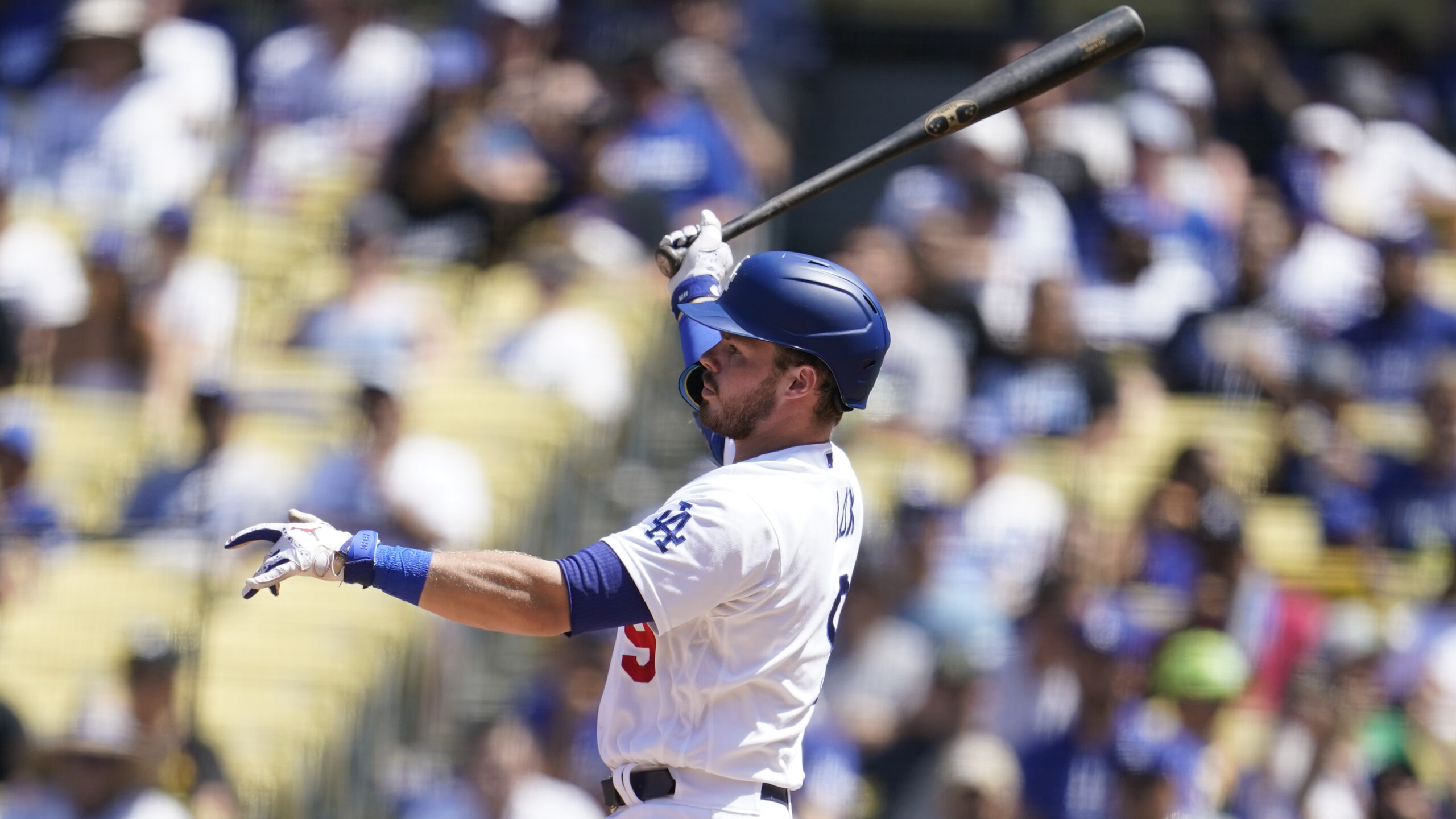 A baseball player swings his baseball bat in front of a blurred stadium crowd