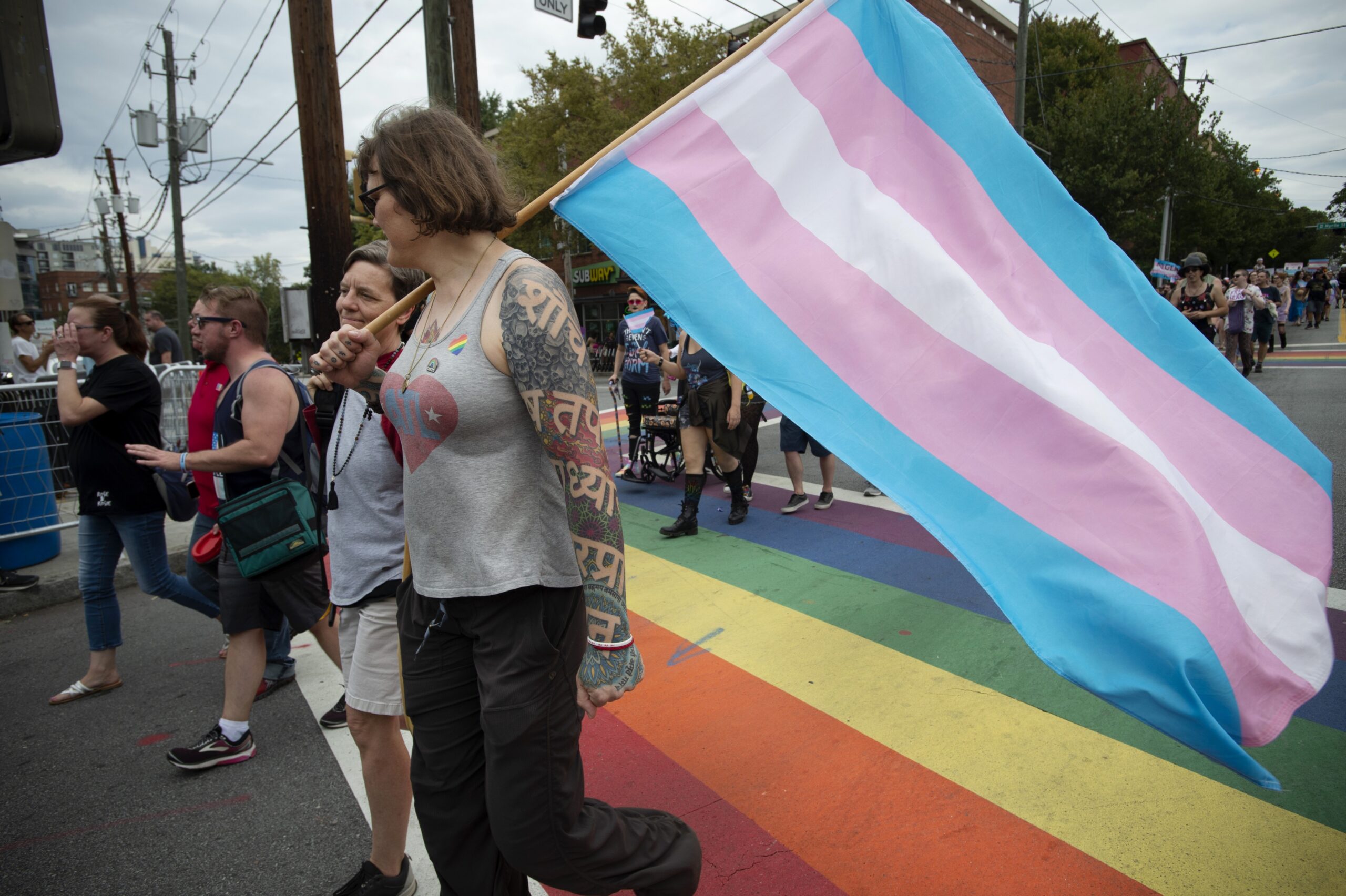 Marchers in an LGBTQ+ pride parade with a transgender pride flag