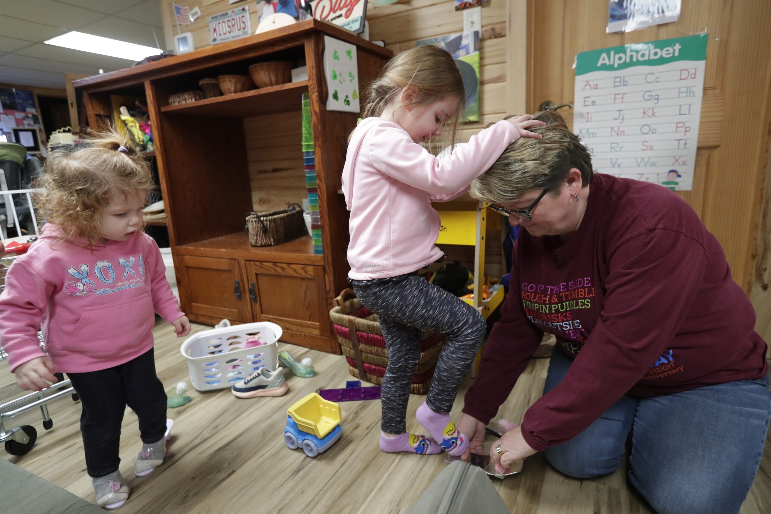Two toddlers try on dress up shoes with the help of their teacher