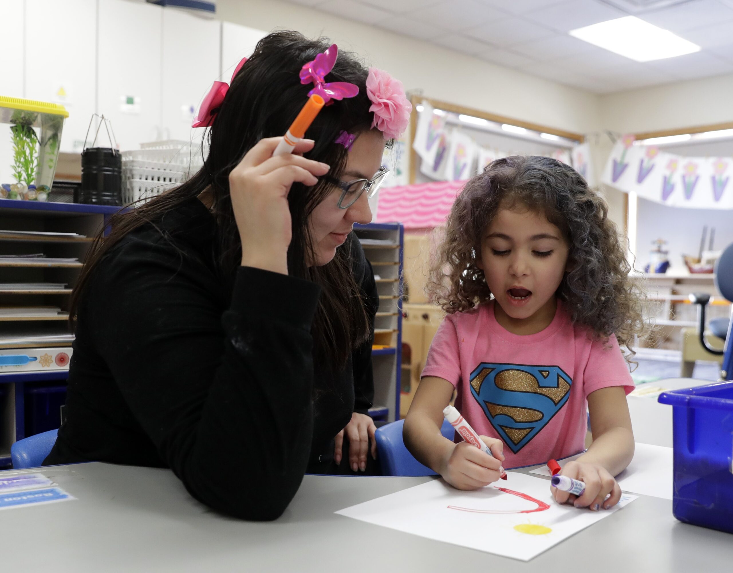 A teacher and her daughter color together in a classroom