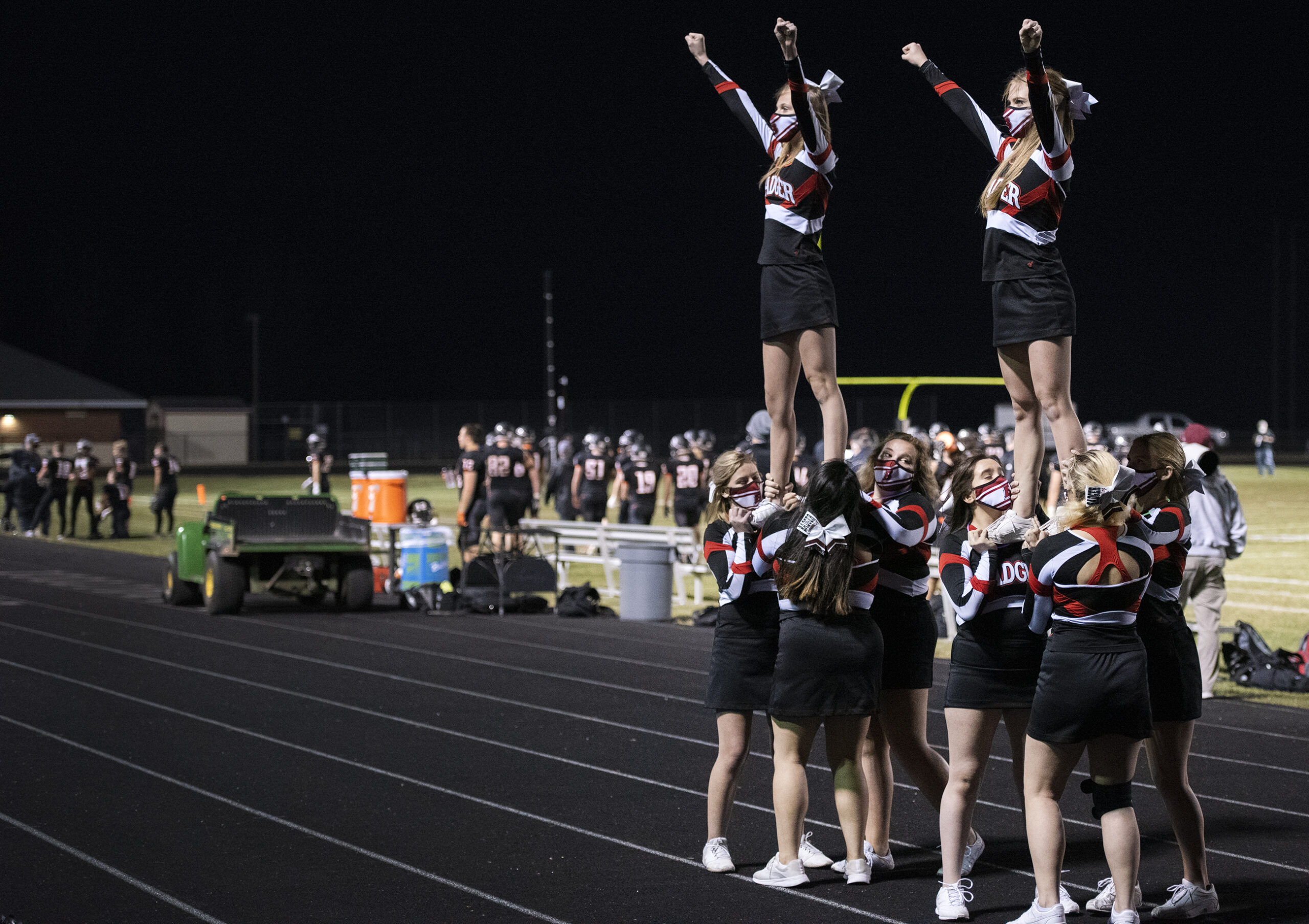 cheerleaders make a formation as they perform on a track surrounding the football field