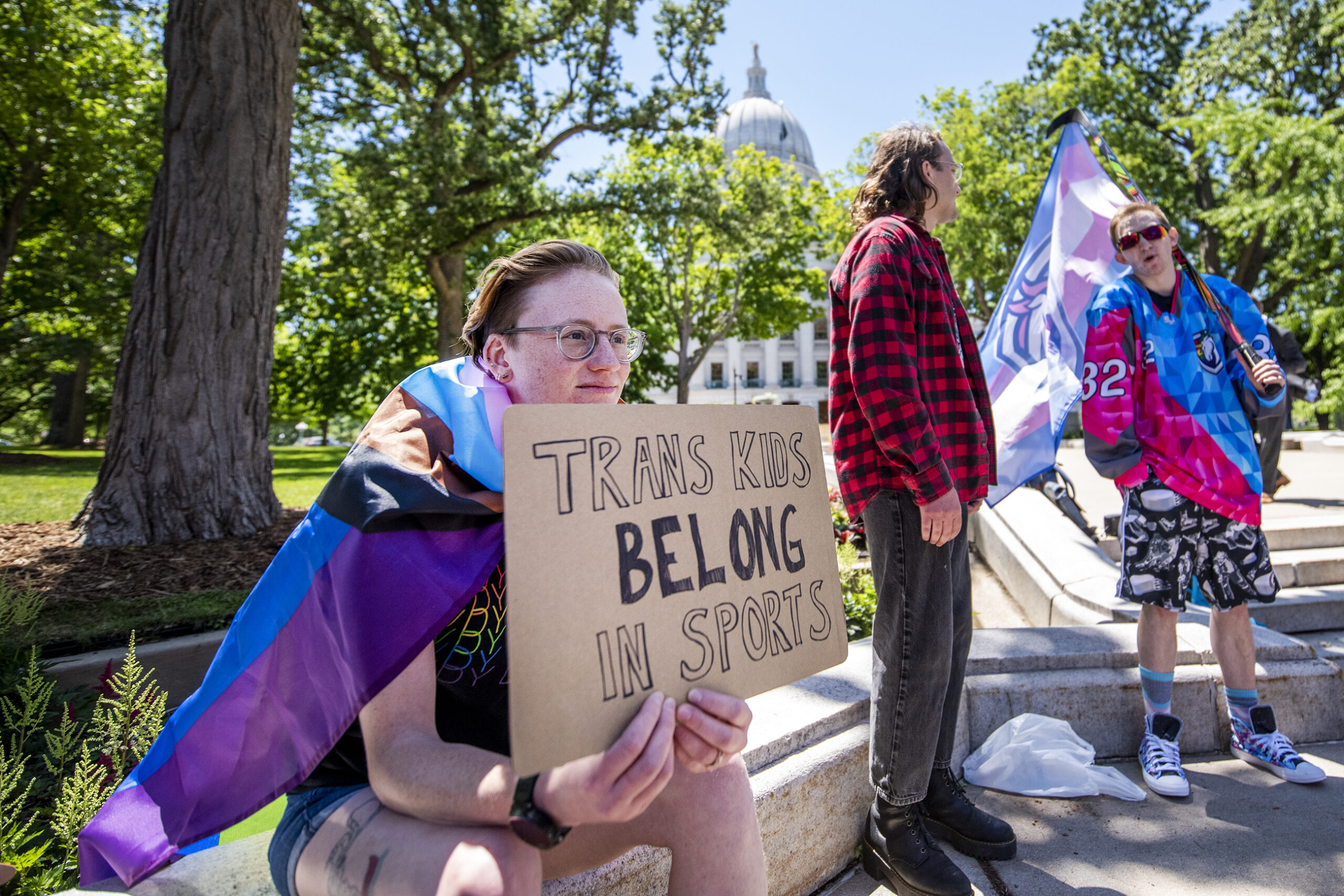 A protester holds a sign that says "Trans Kids Belong In Sports."