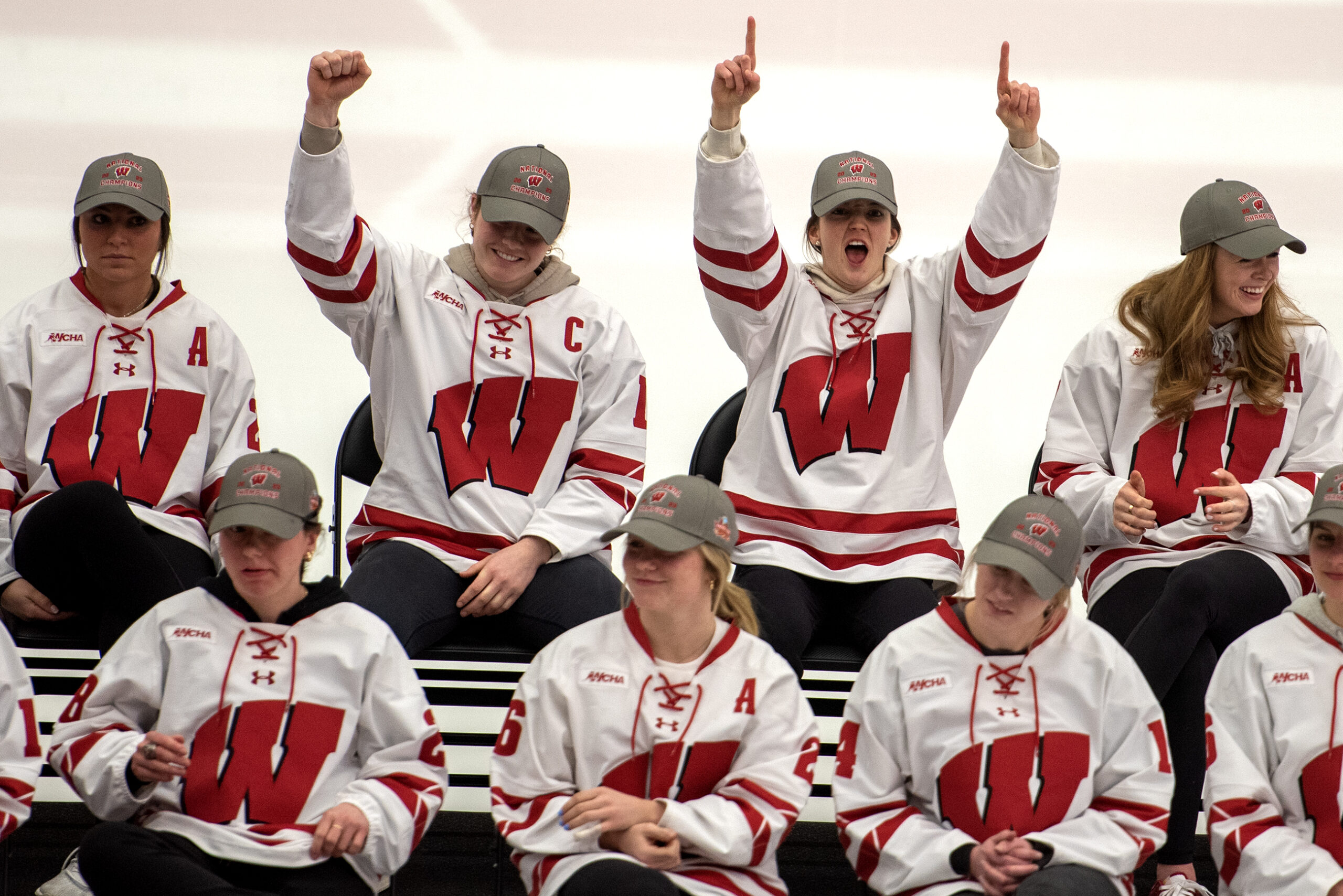 Hockey players sit together in their jerseys on the ice. Two players raise their hands in celebration.