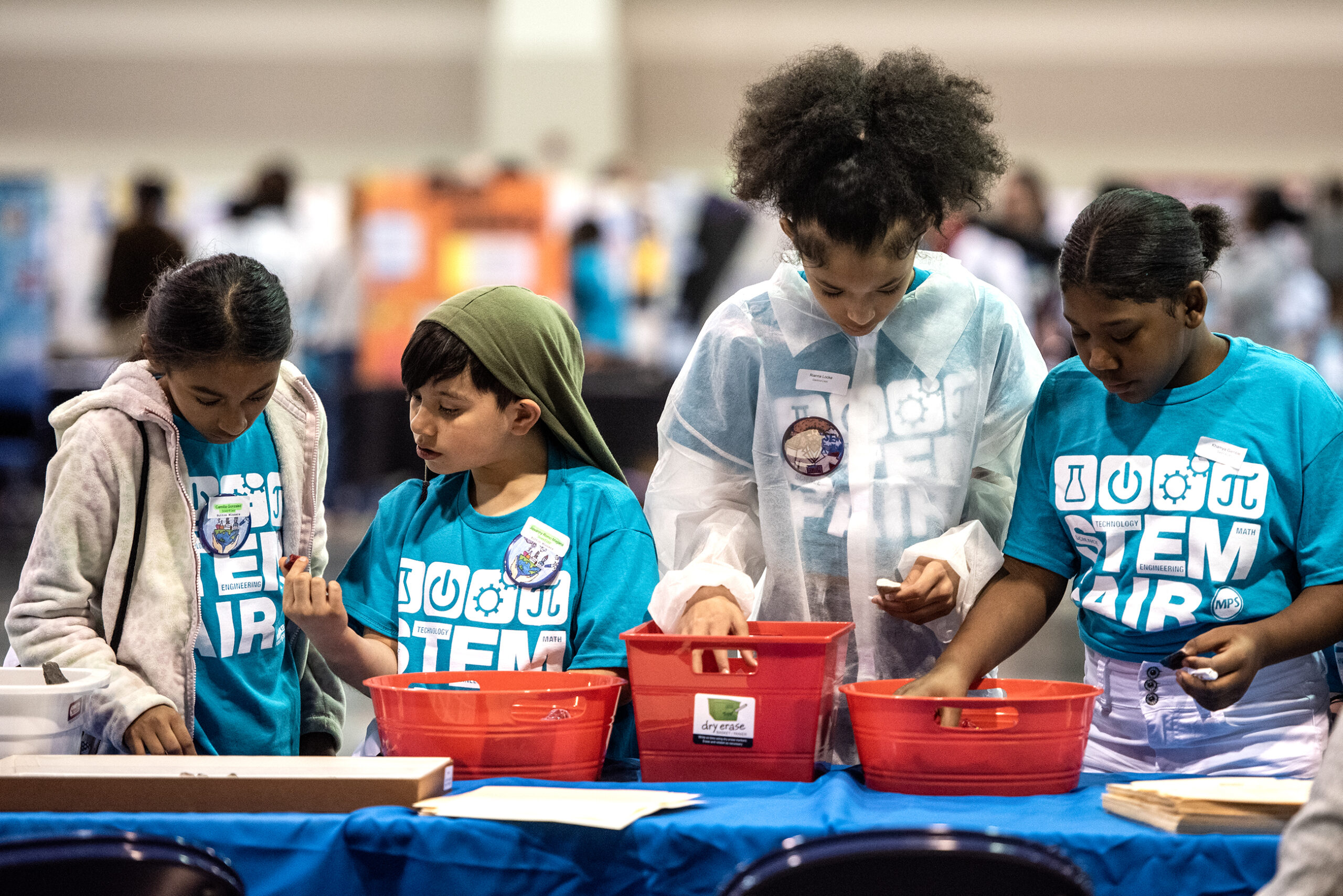 Students stand in front of a table and reach into red bins.