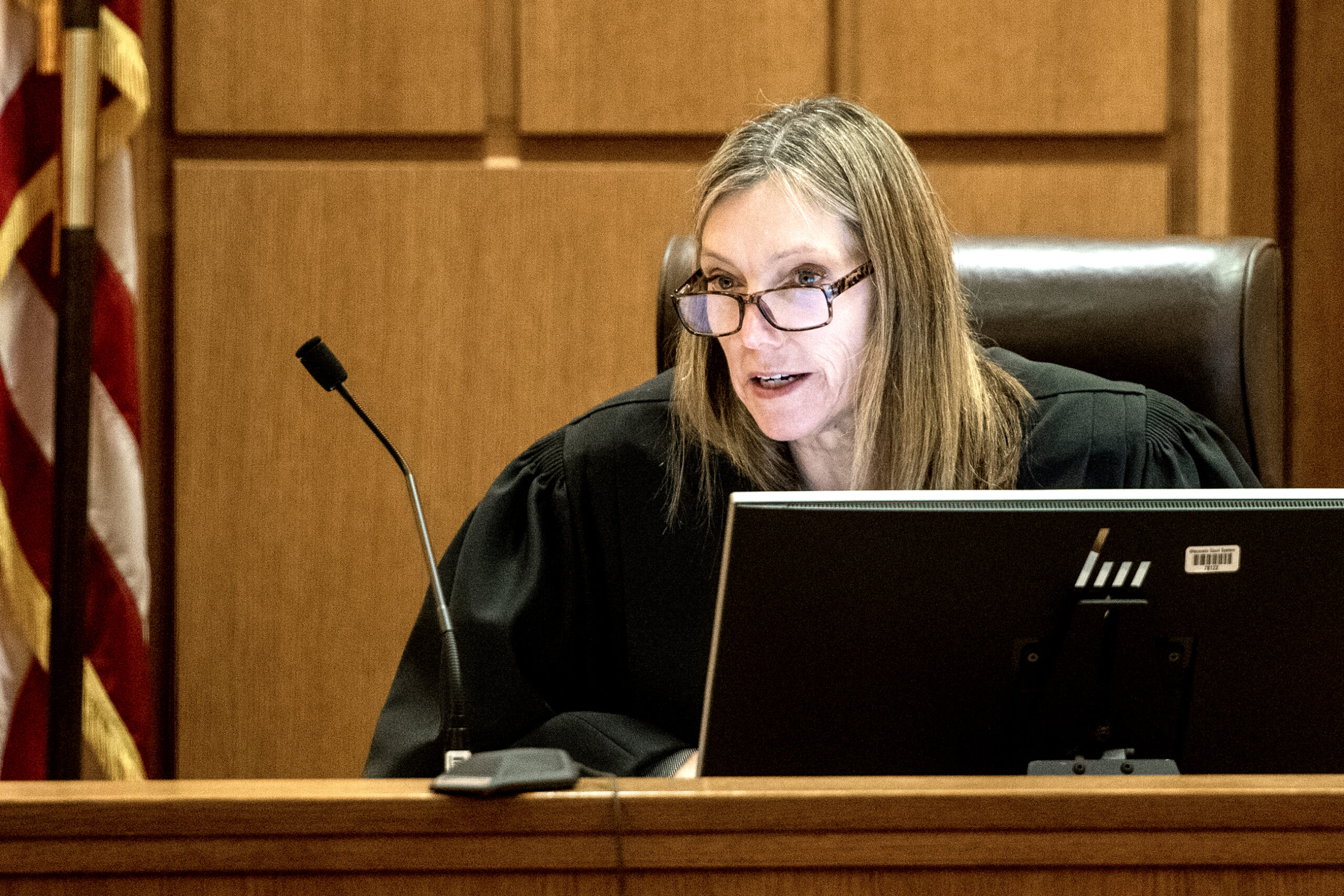 A judge in a black robe sits at the front of a courtroom.