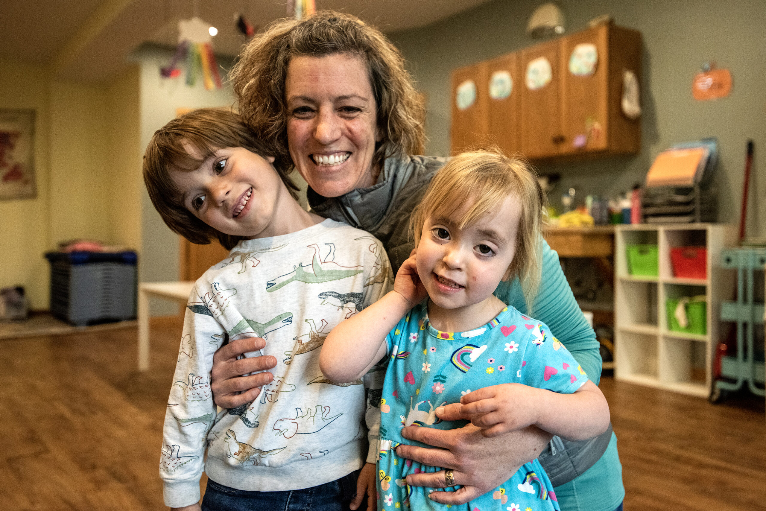 A mother holds her two small children in a classroom.