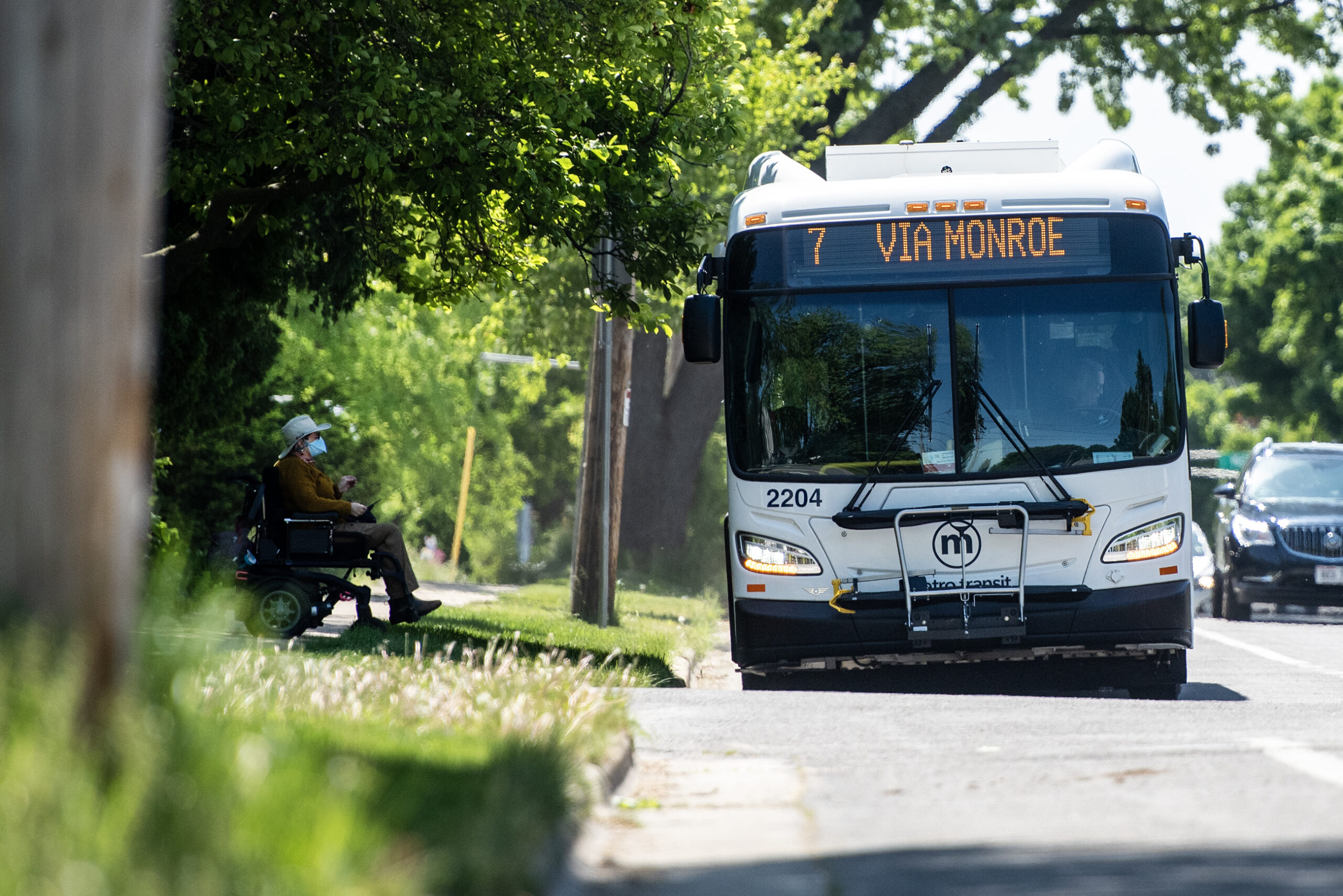 A bus lowers itself to allow a passenger waiting on a sidewalk in a wheelchair to board.