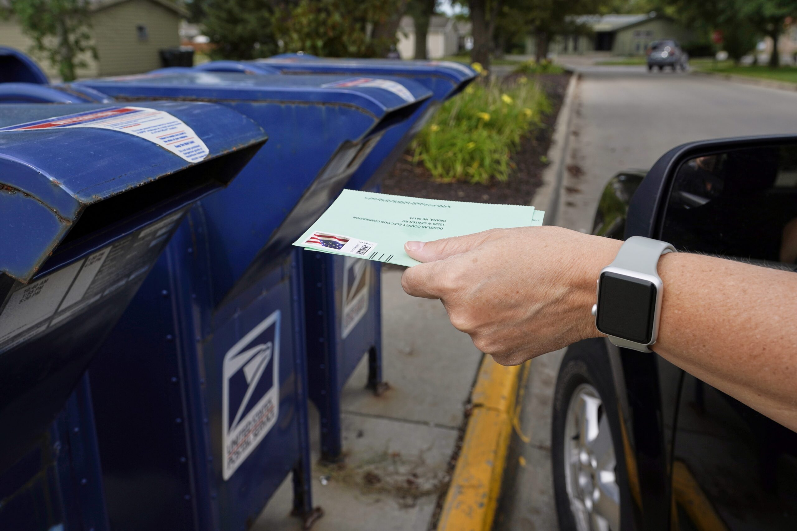a person drops applications for mail-in-ballots in a mailbox