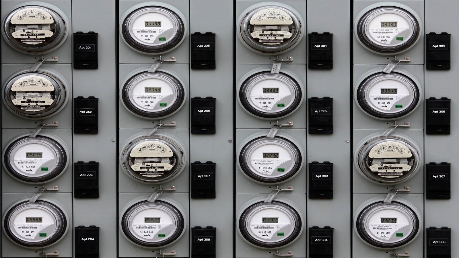 A grid of electric utility meters and labeled black circuit boxes mounted on a gray panel, each meter displaying numerical readings.