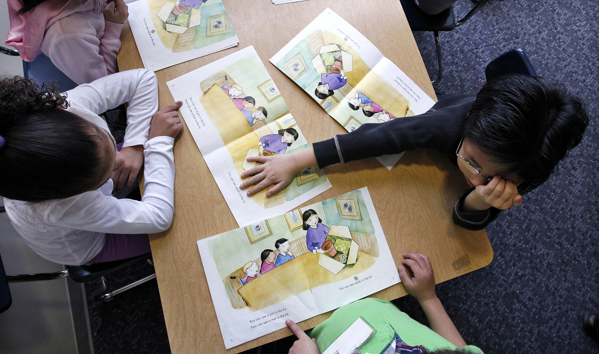 Kindergarteners read books at their desks during class.