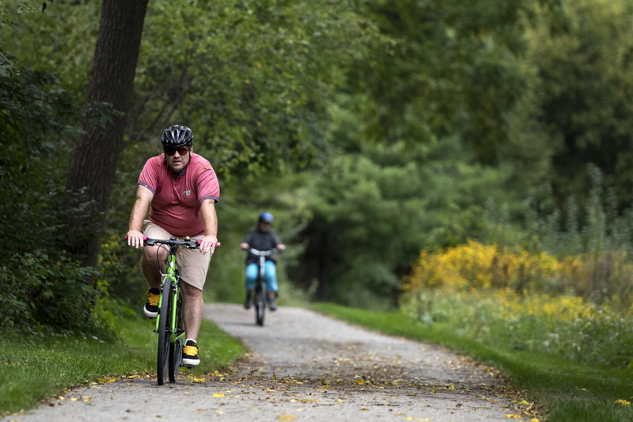 Two bicyclists ride on a paved section of the Ice Age Trail surrounded by greenery
