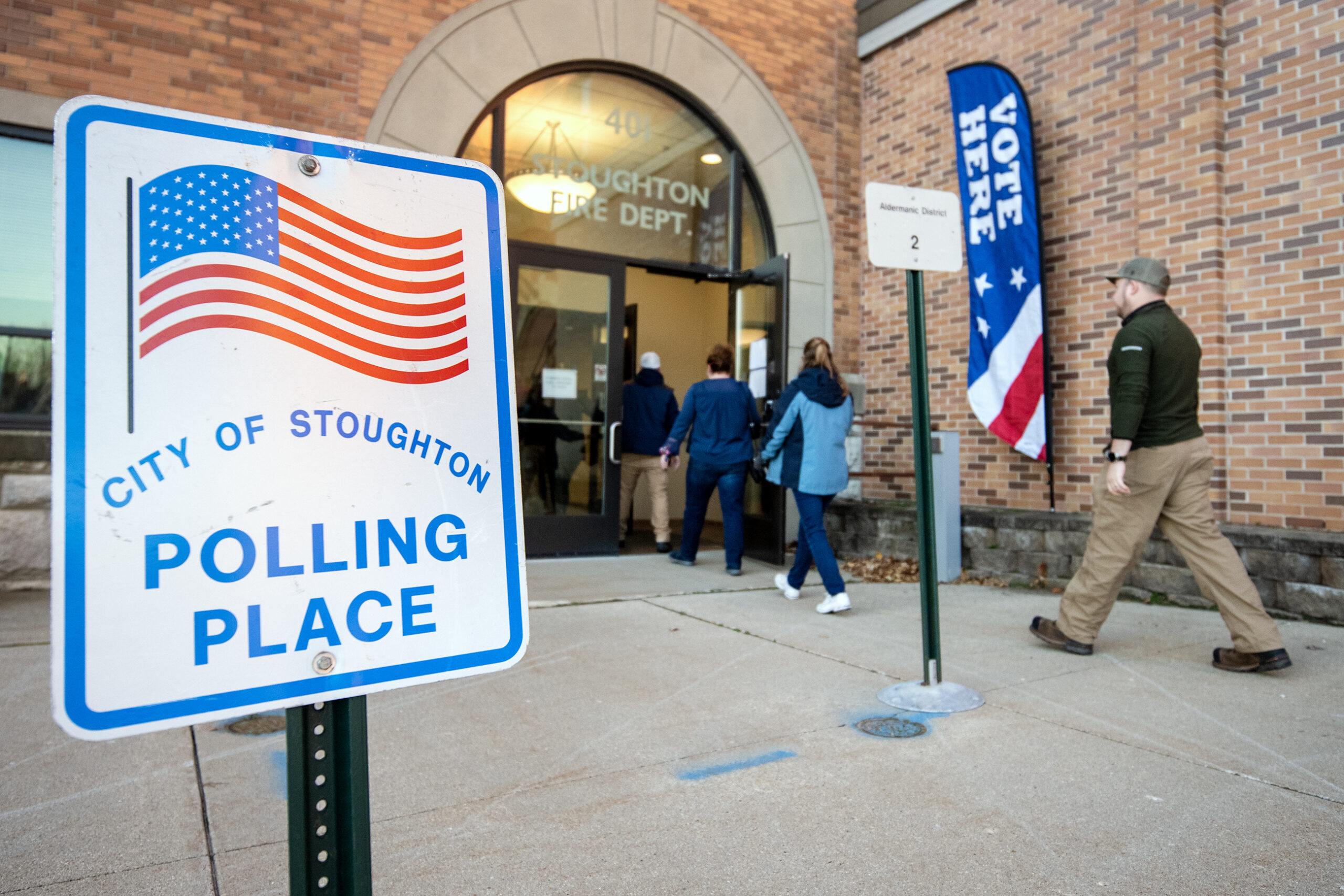 A line of voters walk past a sign that says "City of Stoughton Polling Place"
