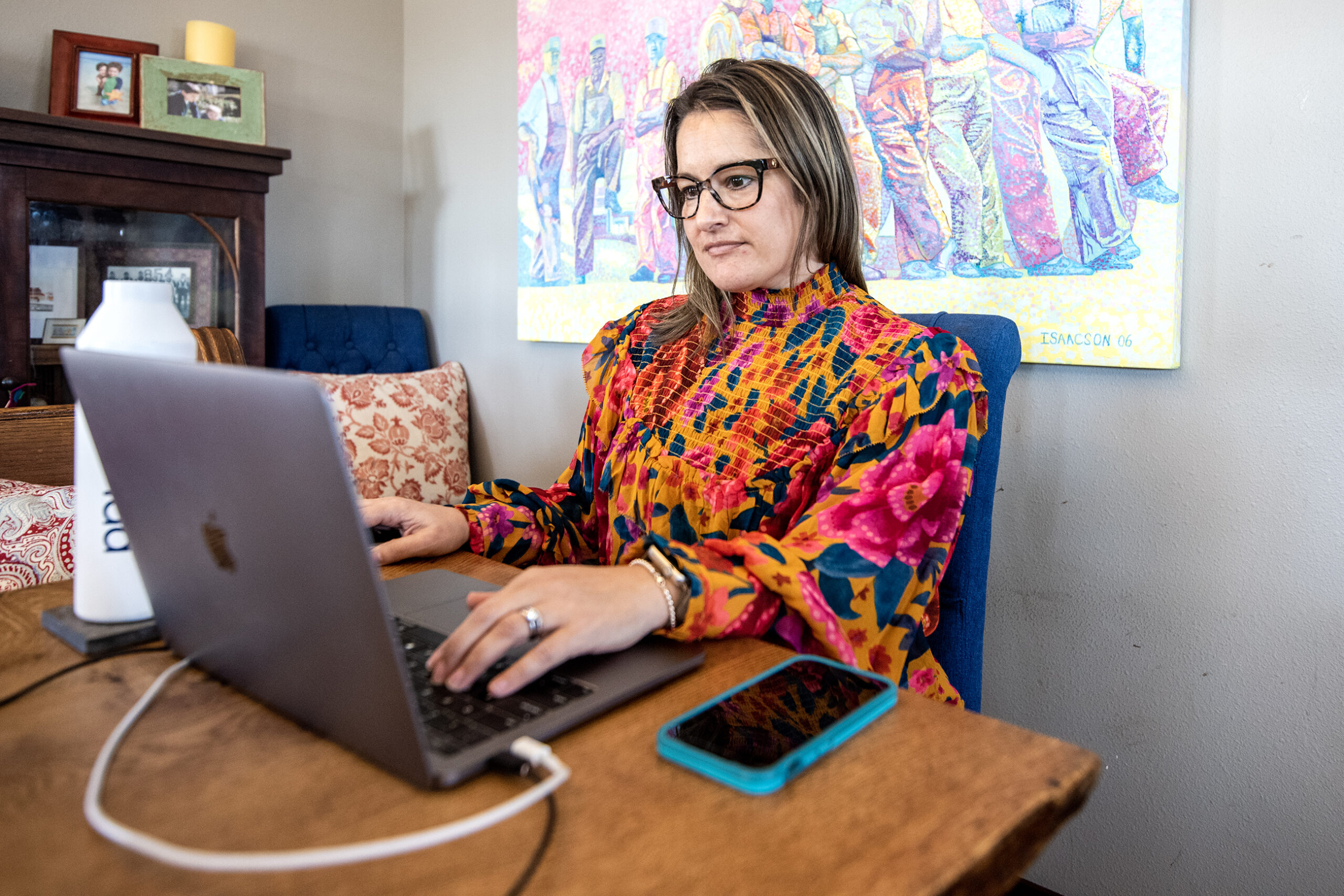 A woman sits at a table in front of a laptop.