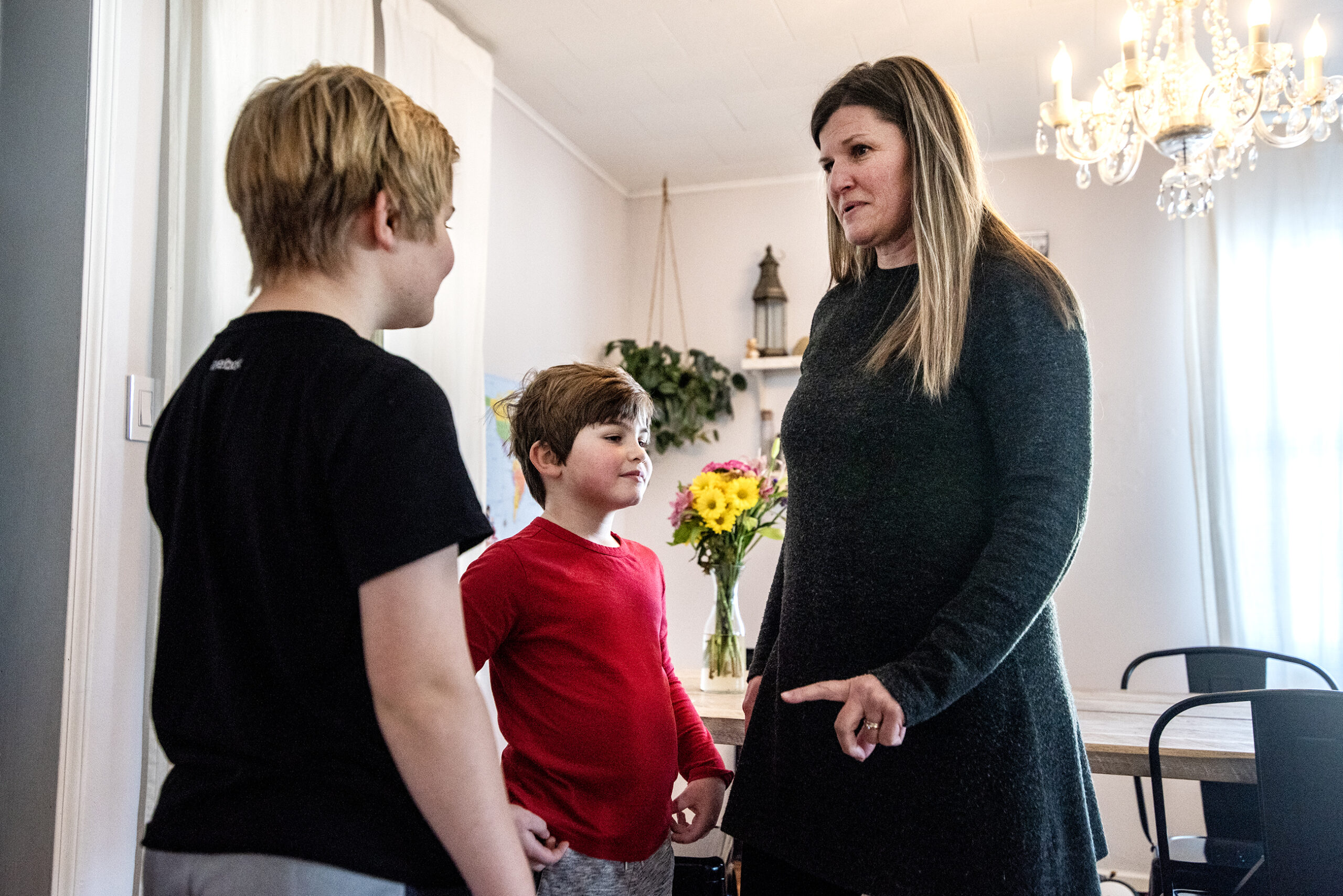 A woman stands with her two children in a dining room.