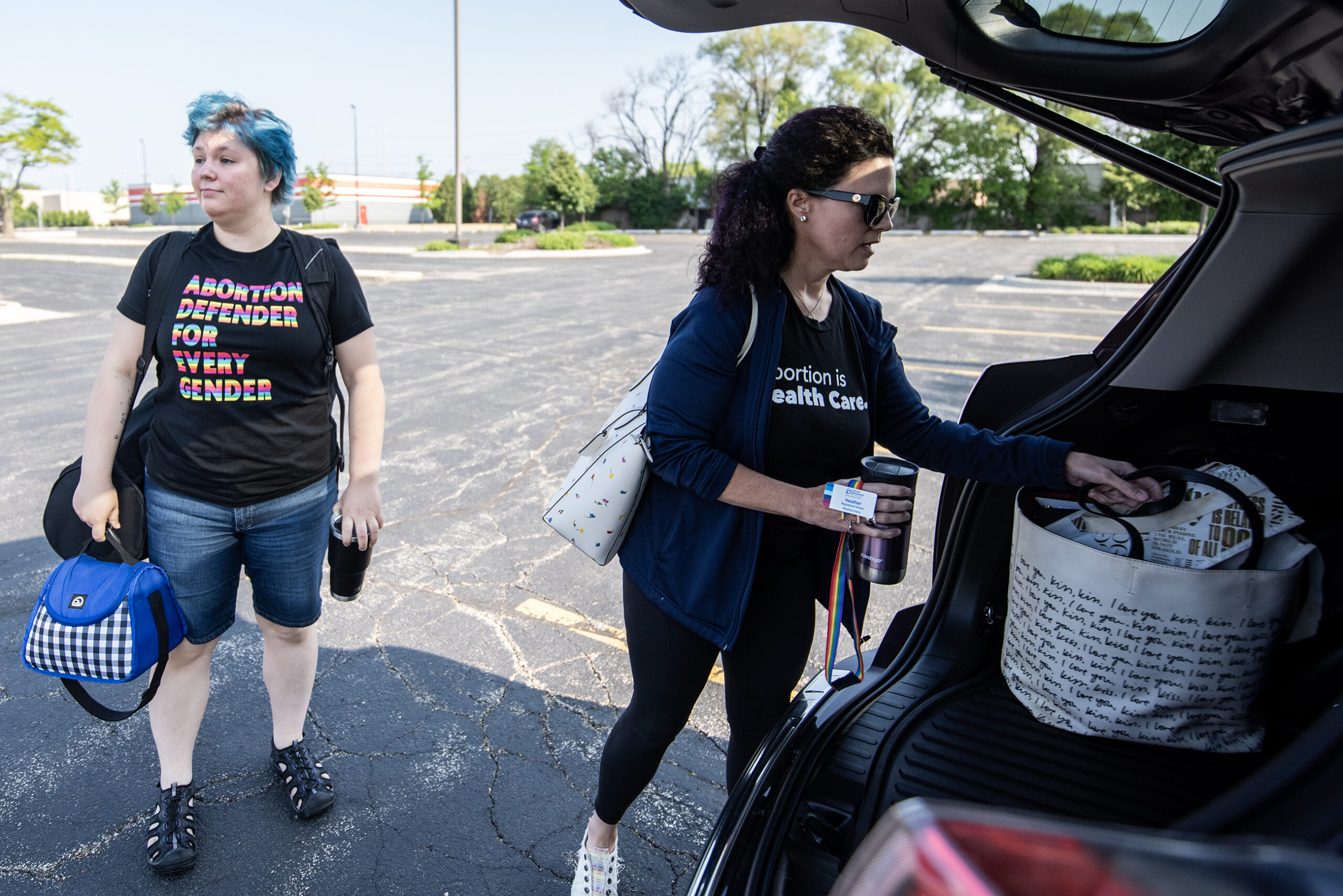 Two people stand near an open trunk as they hold bags of belongings.