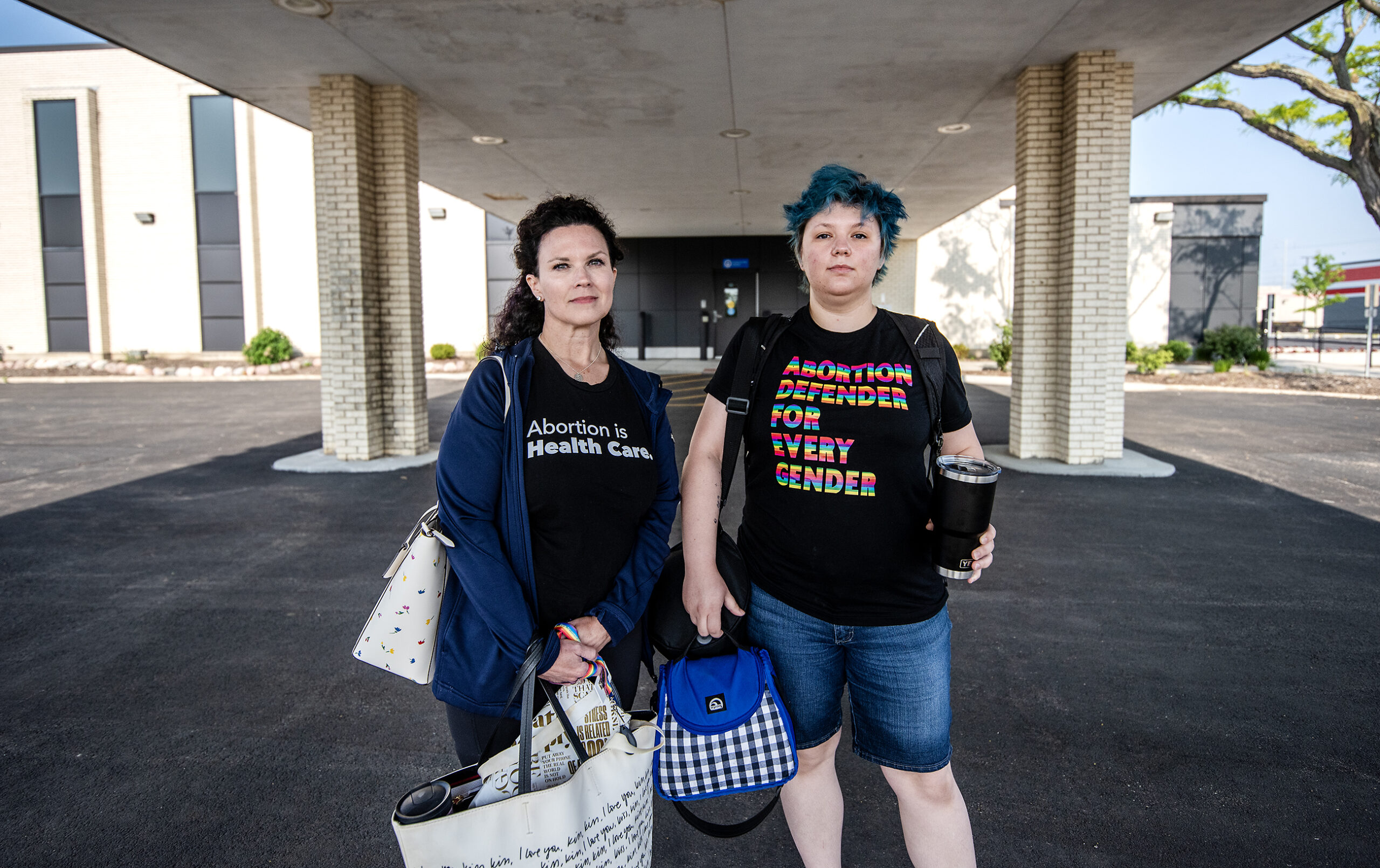 Two people stand with bags at the entrance to a building.
