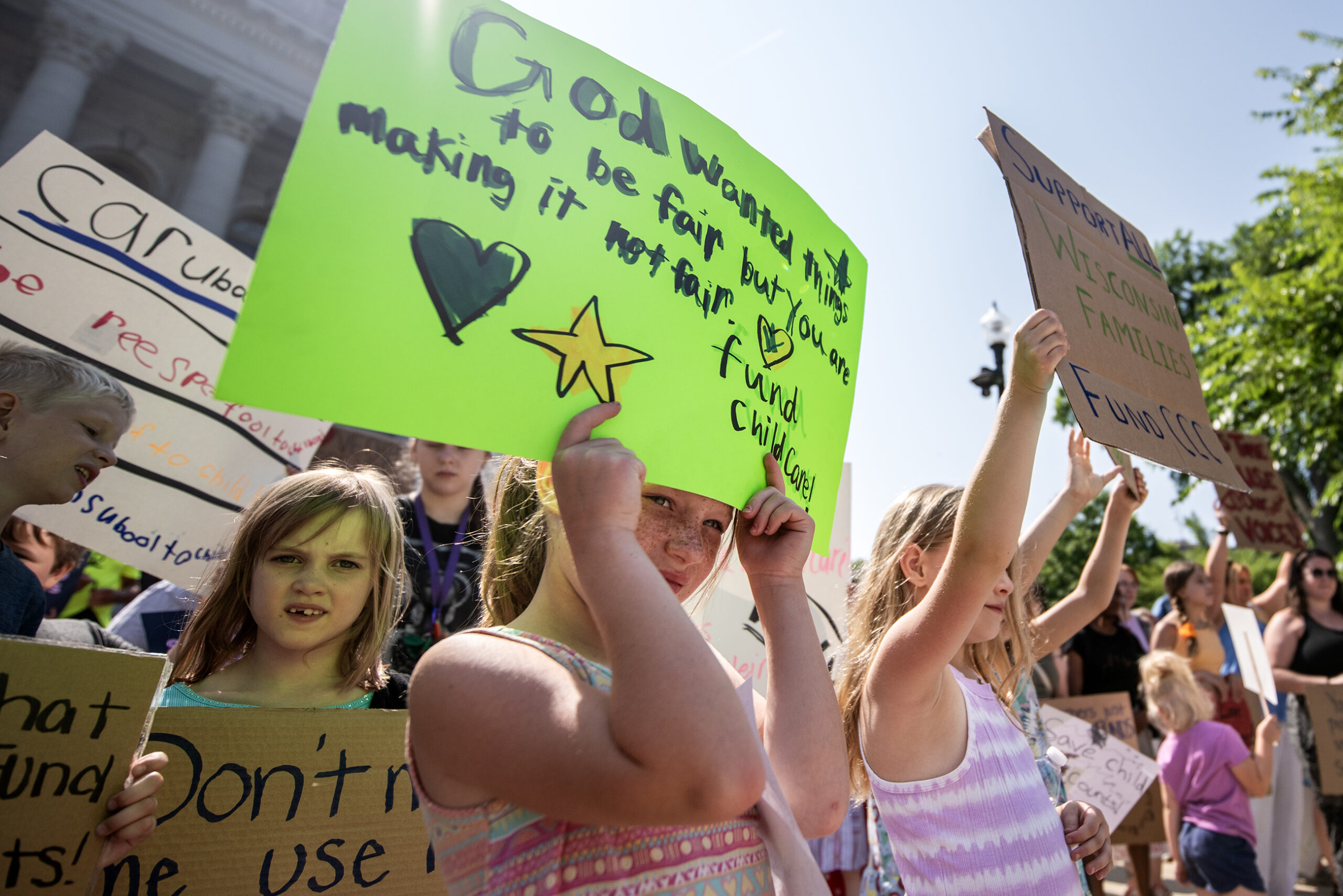 A child holds a green sign above her head in a crowd with other children holding signs.