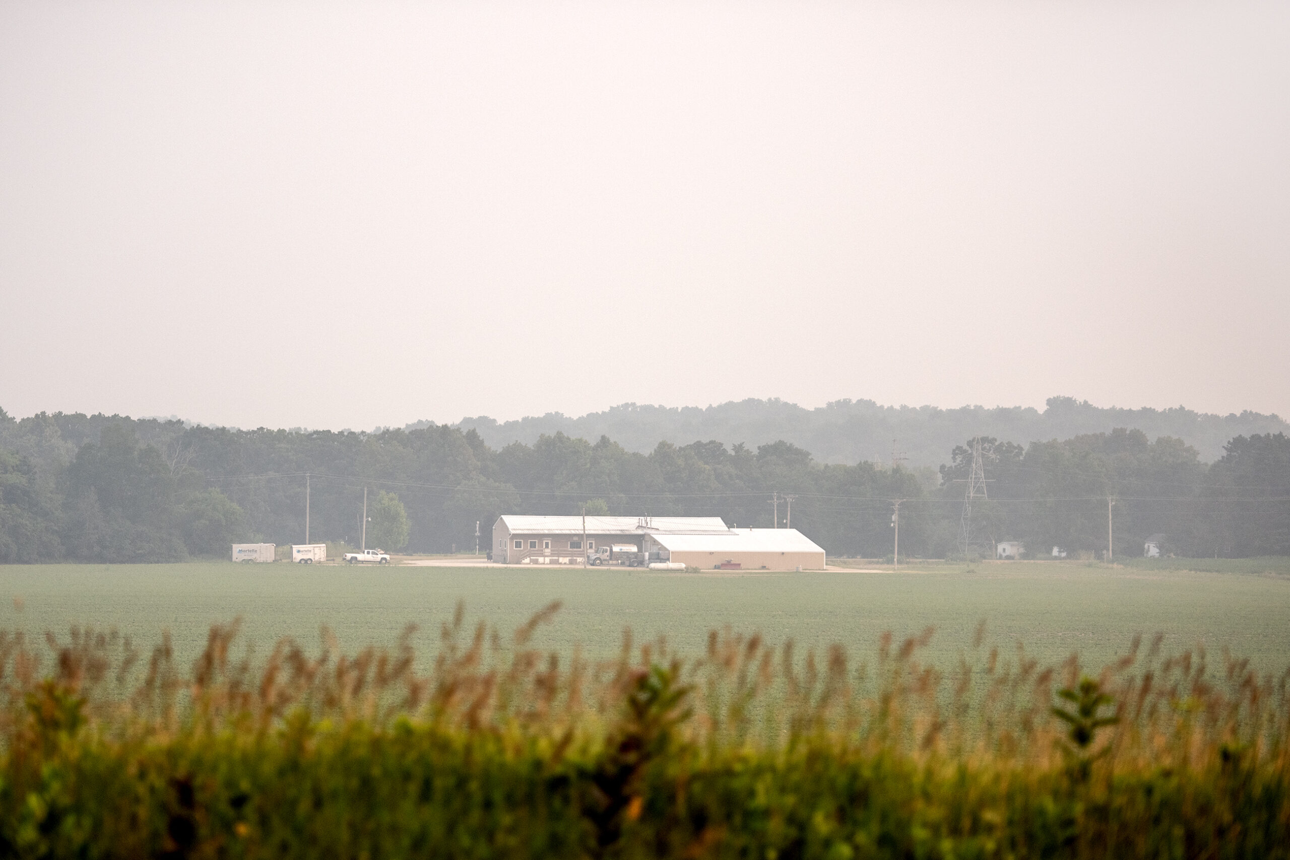 A farm in the distance is clouded by white smoke.