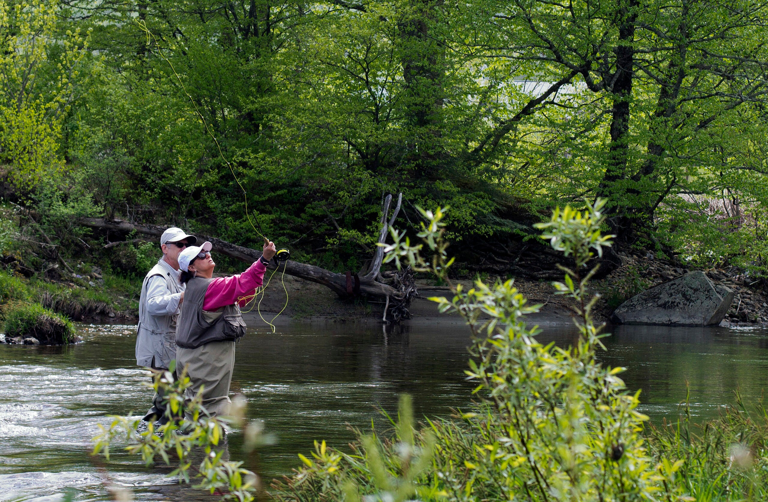 Two people fly fish in a river.