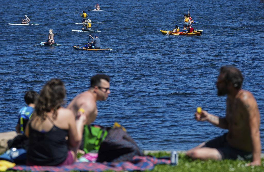 Sunbathers chat as paddleboarders and kayakers enjoy the waters of Lake Union, Saturday, May 13, 2023, in Seattle. Saturday's temperatures reached record-breaking highs for several cities across western Washington, with a heat advisory in effect until Mon