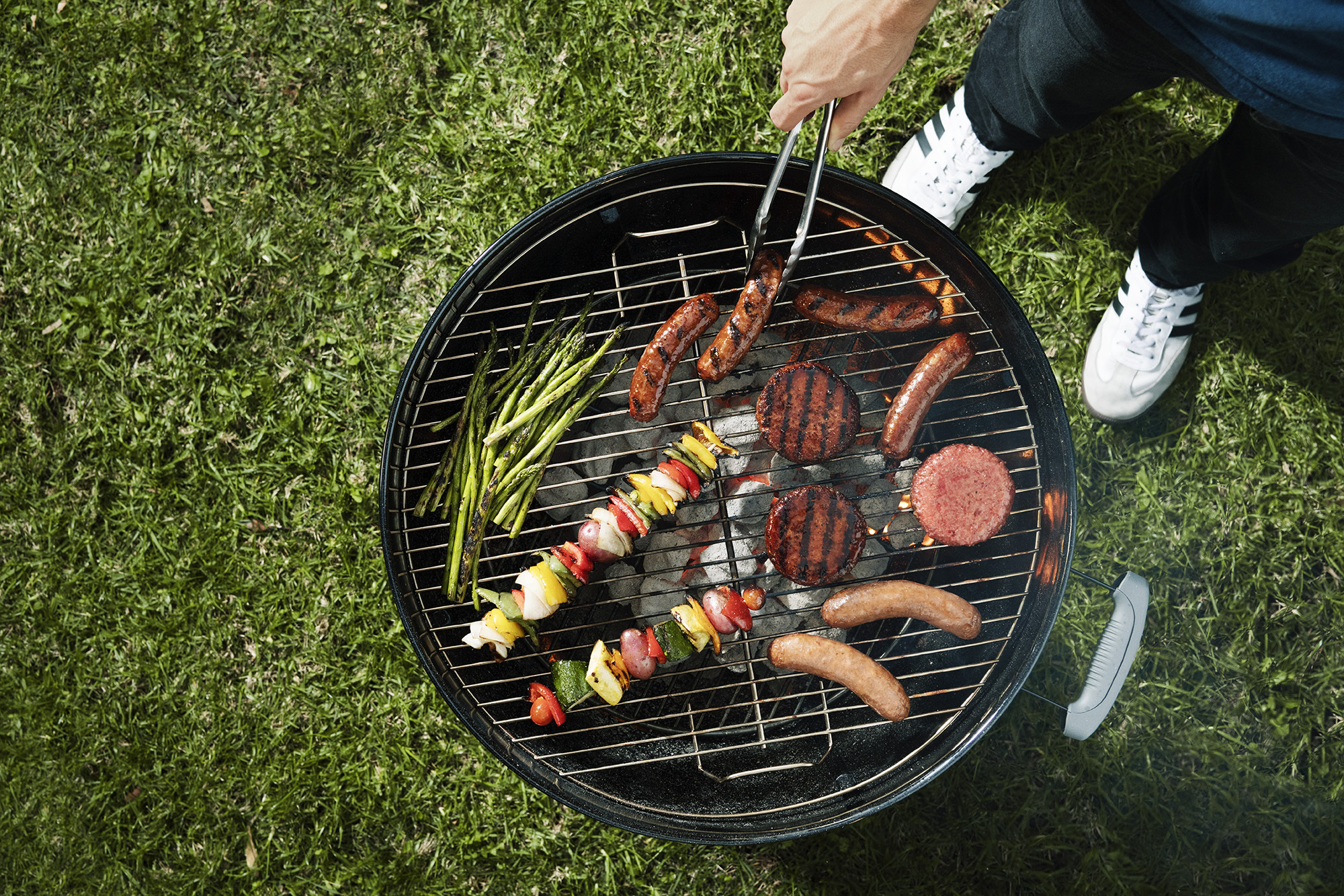 A man uses tongs to rotate food on a grill.