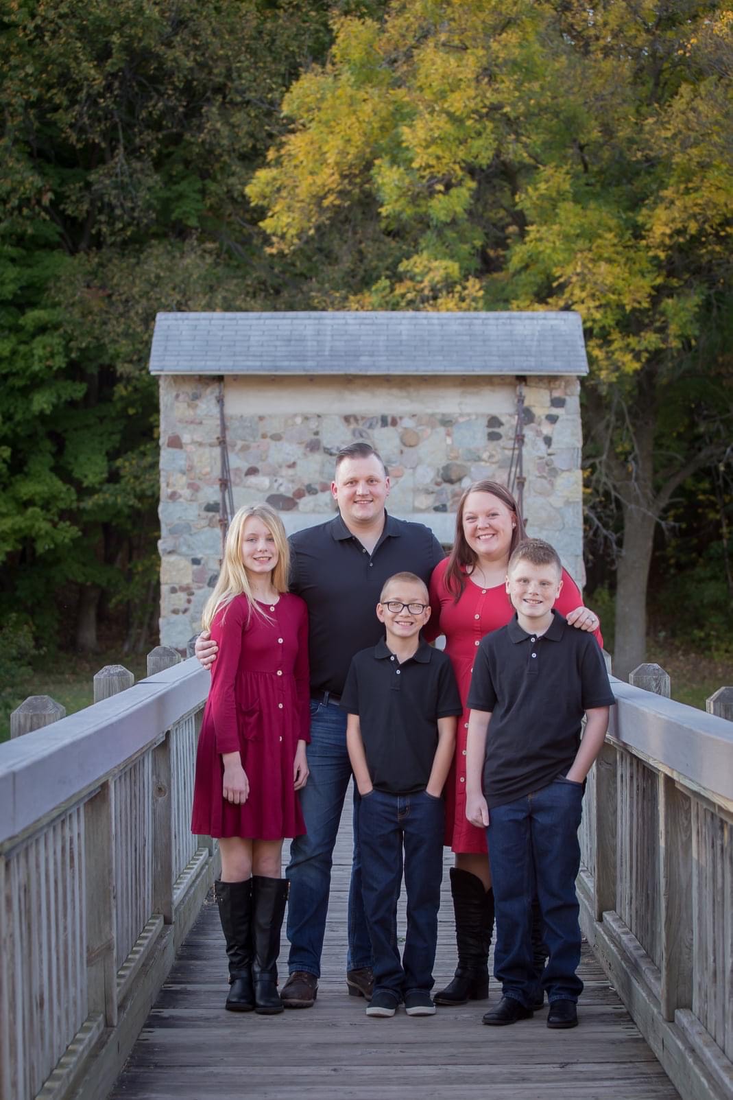 A family of five poses on a bridge with trees in the background