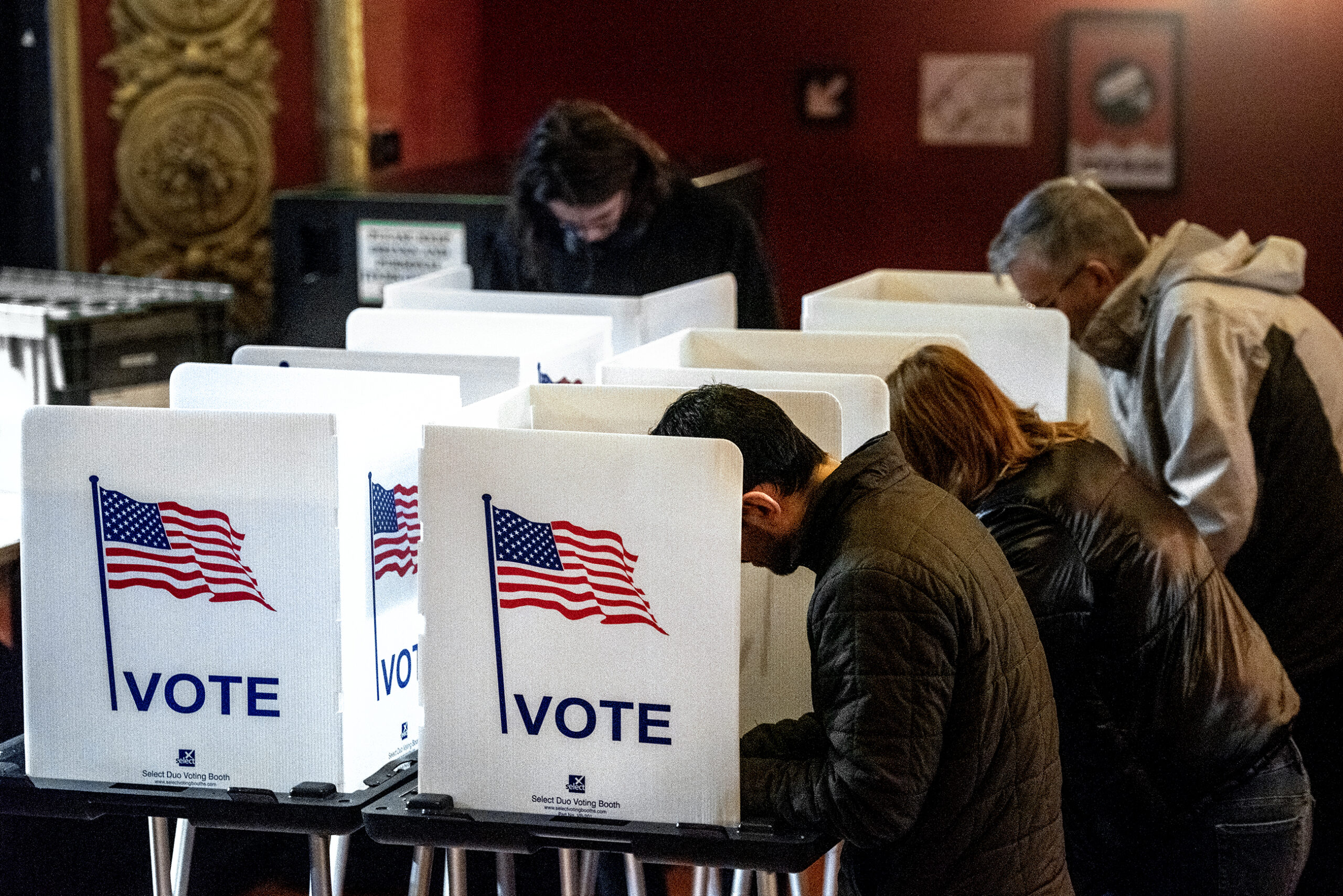 Four voters lean over as they fill out their ballots behind dividers that say 