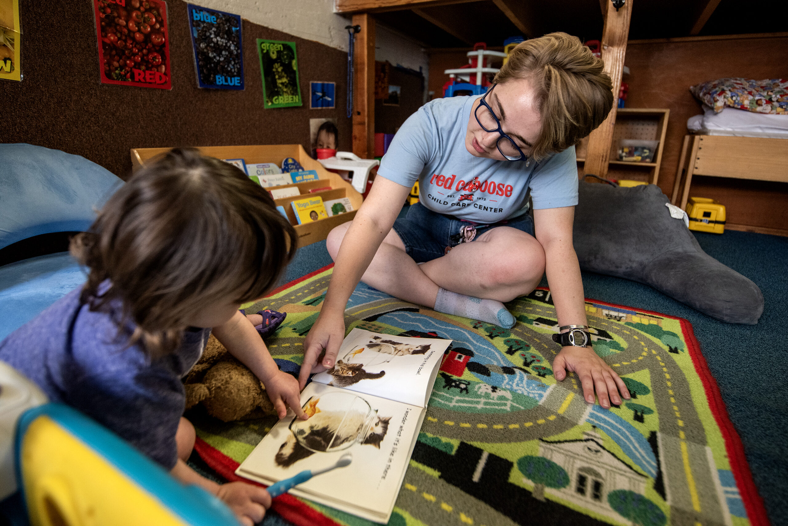 A teacher sits on the floor with a child as they look at a book together.