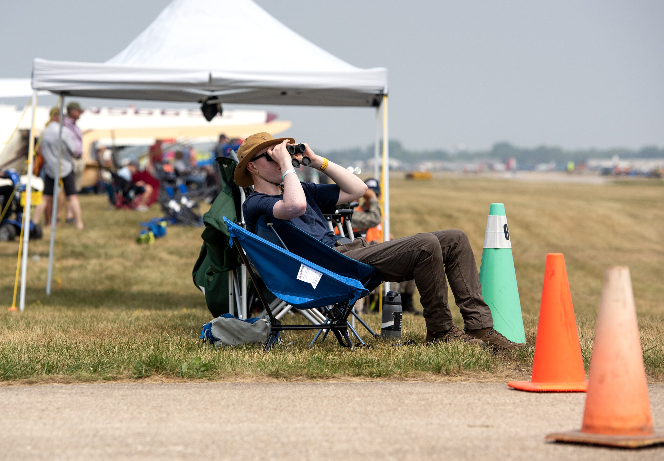 A man sits in a lawn chair and looks up using binoculars.