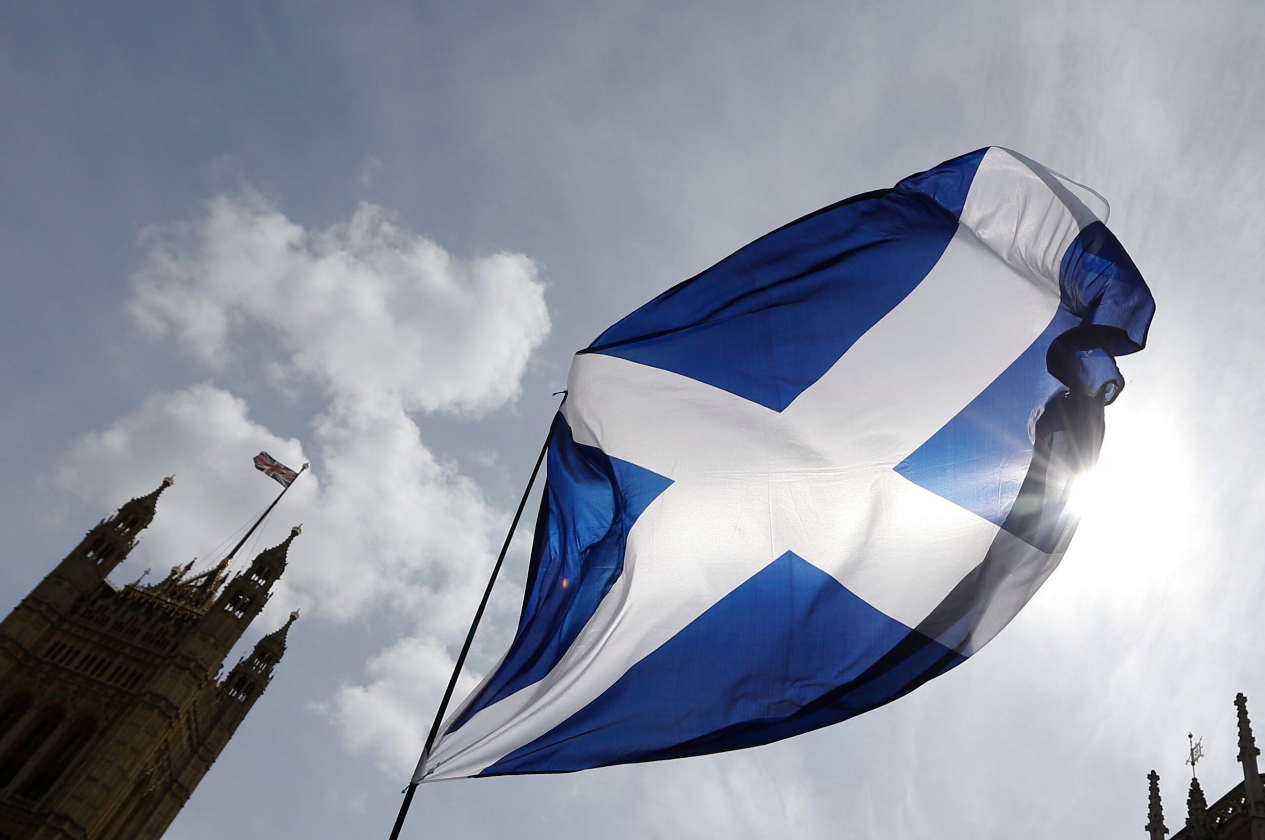The Scottish flag flies in the sun. The roof a castle is in the corner of the picture