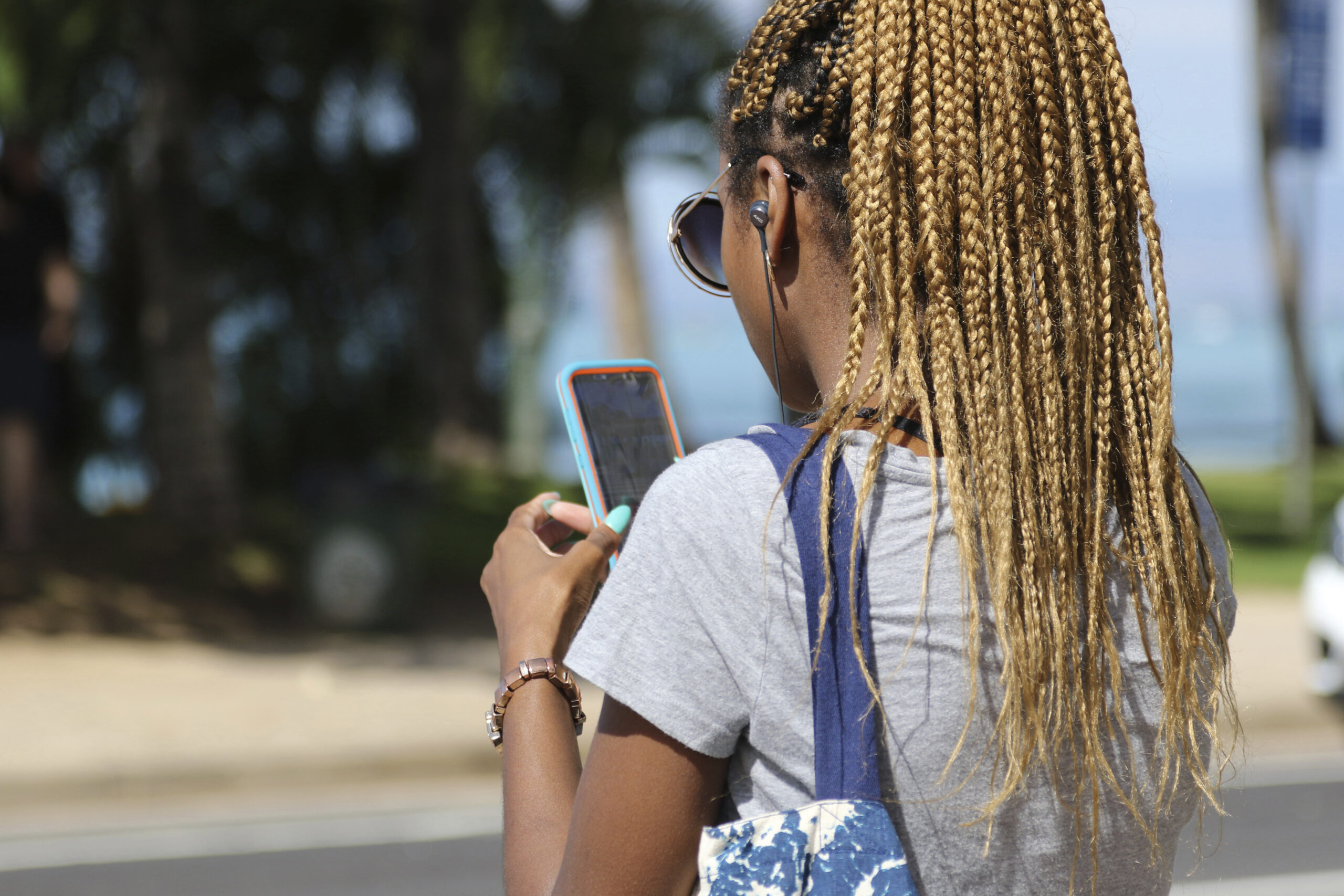 A woman walks away from the camera. Over her shoulder, it's seen that she's looking at a phone.