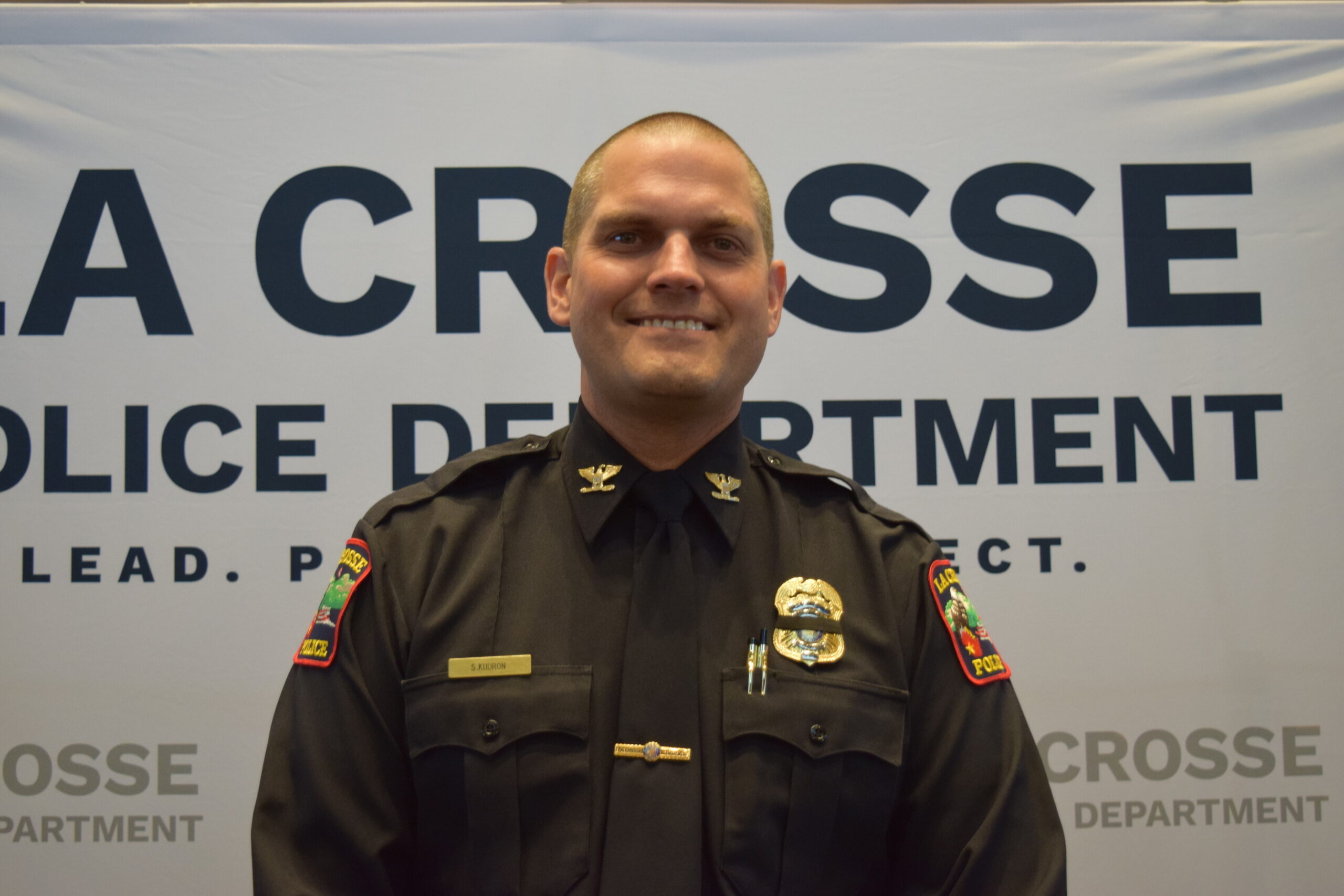 Police Chief Shawn Kudron smiles in front of banner with his department's new brand