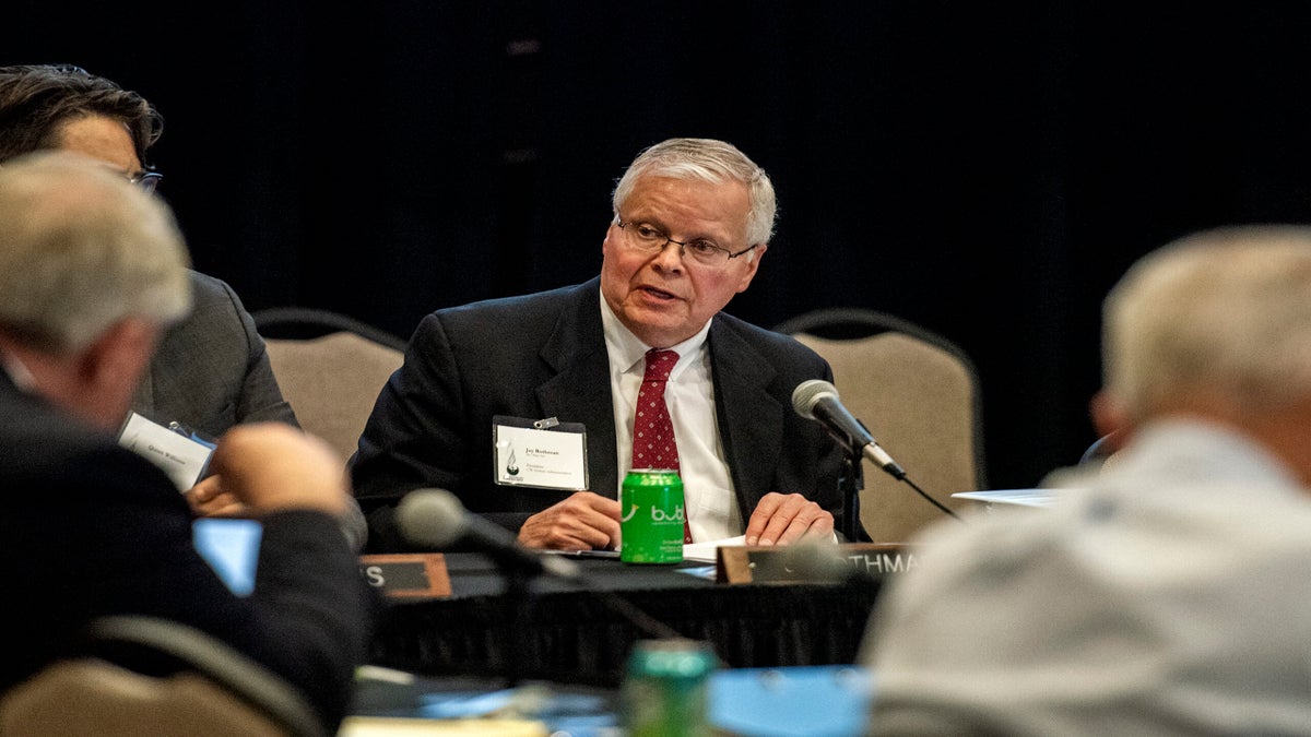 A man looks to the side as he speaks into a microphone.