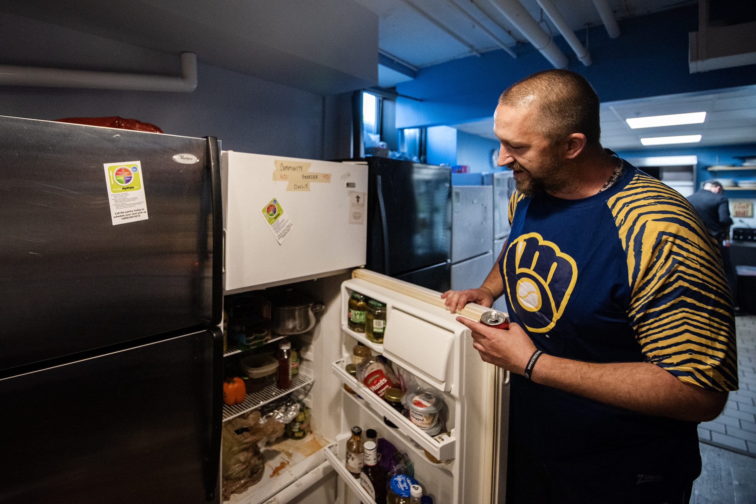 A man gestures as he opens a refrigerator door.