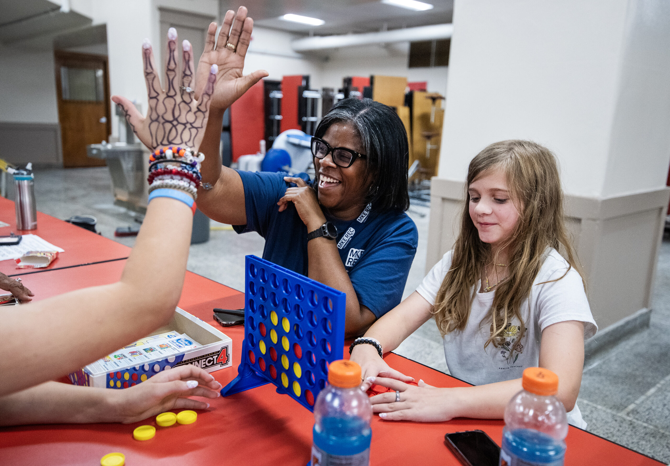 A leader smiles and gives a high five while sitting at a table playing games with students.