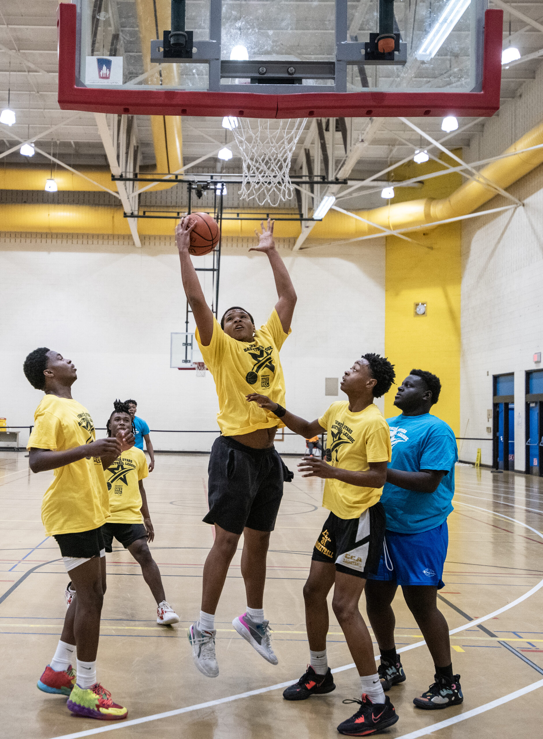 A player in a yellow shirt reaches up to make a layup.