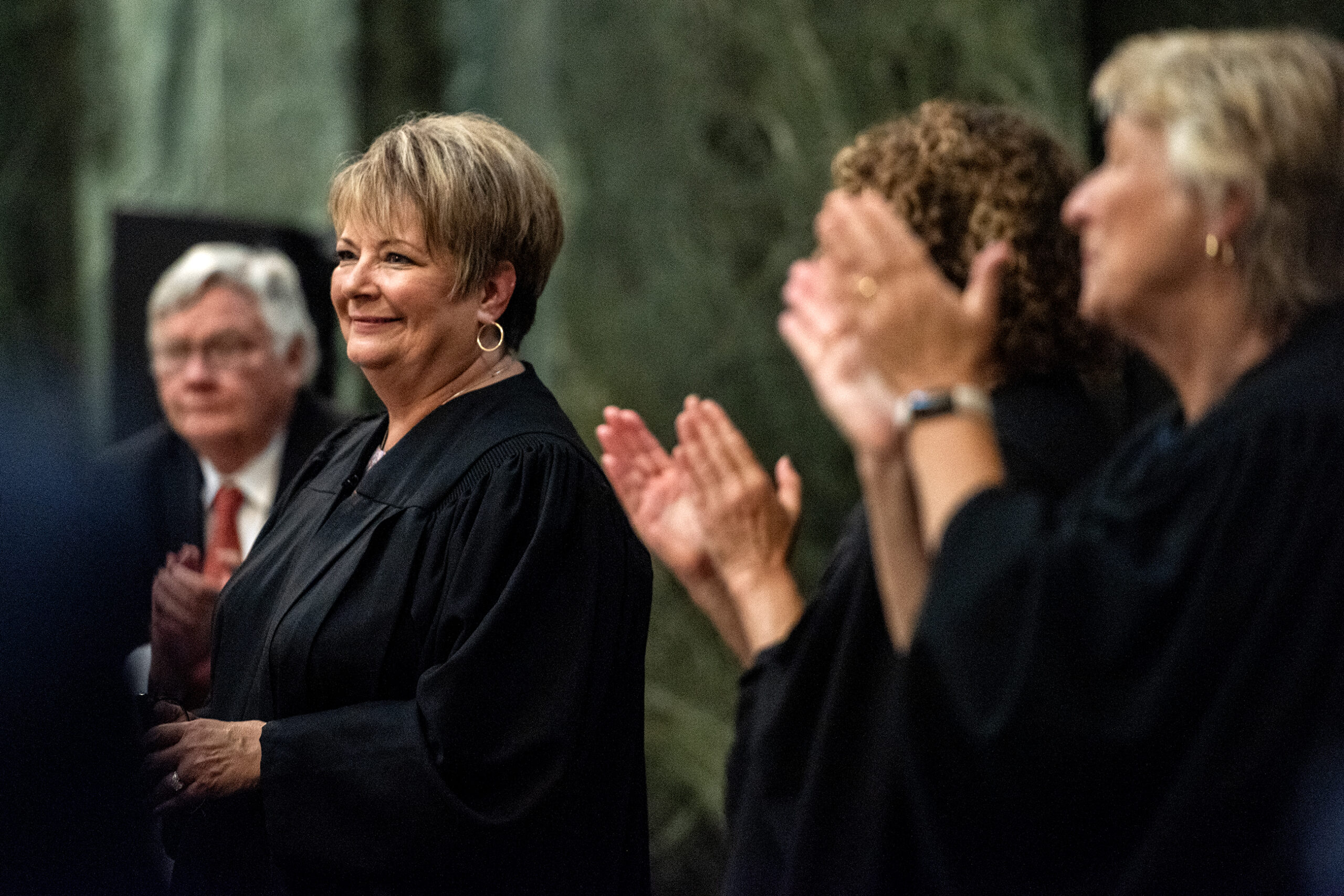 Janet Protasiewicz smiles at the podium as other justices applaud behind her.