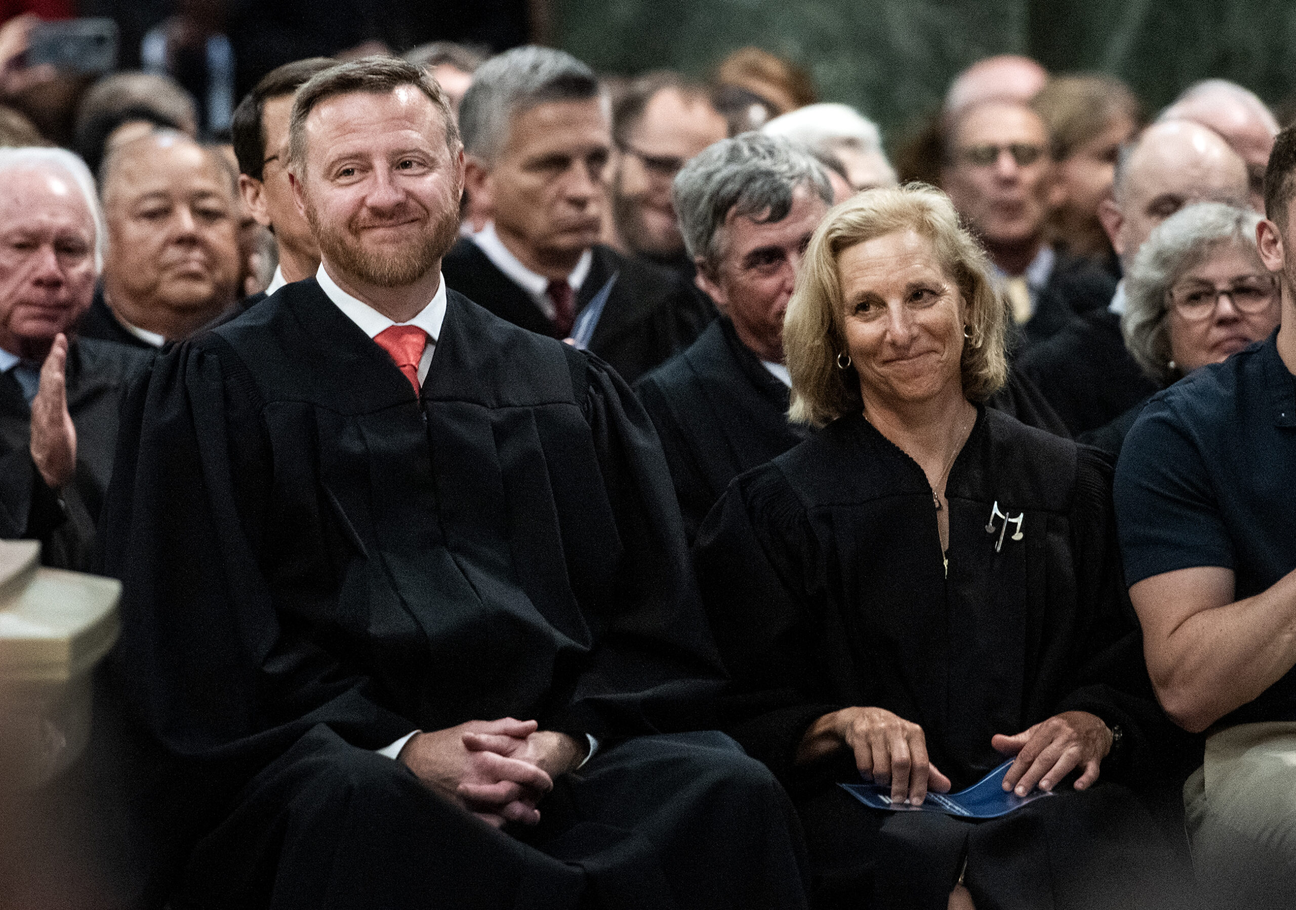 Two justices smile as they sit together in a crowd.