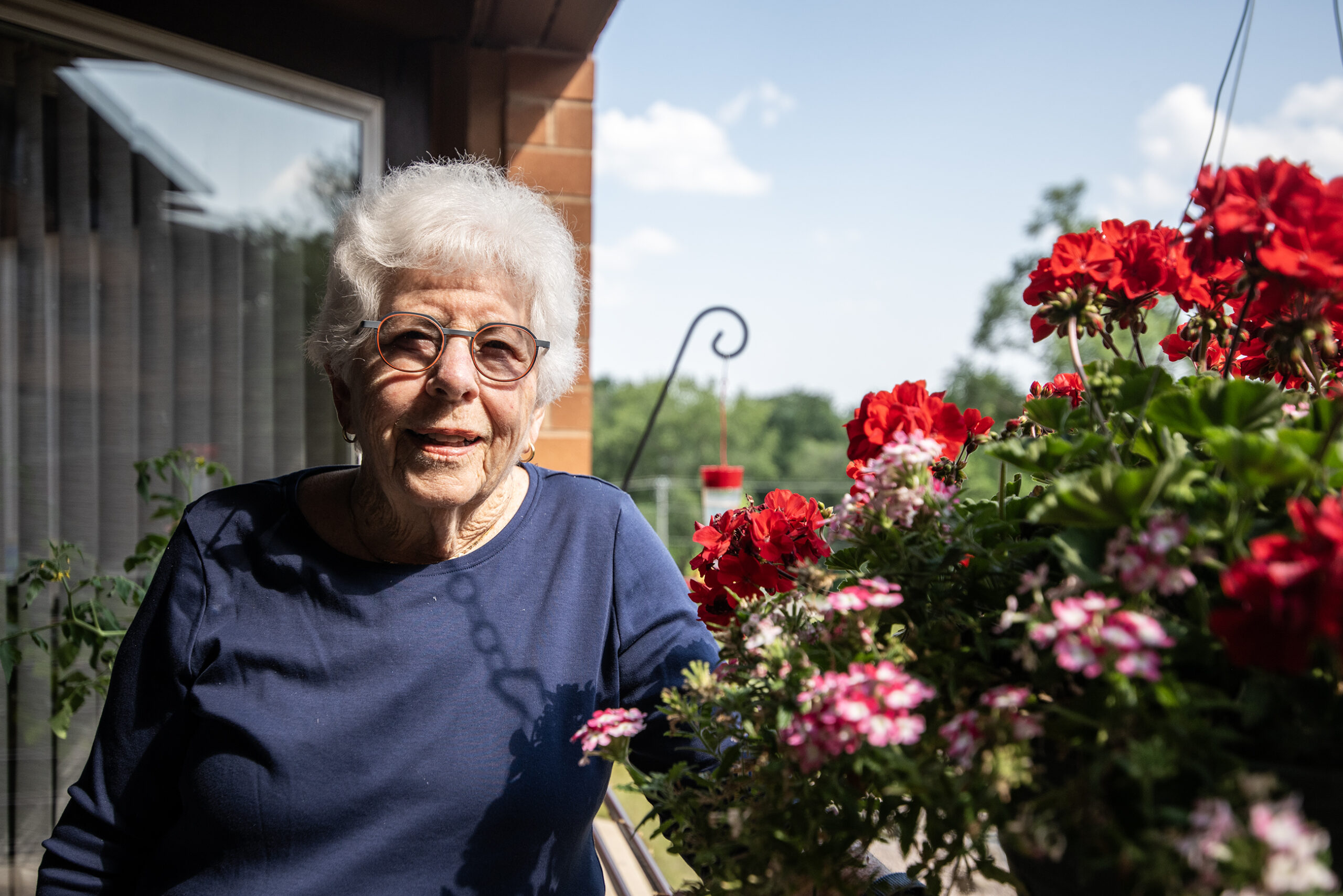 Barbara Lorman stands outside on a balcony near red flowers.