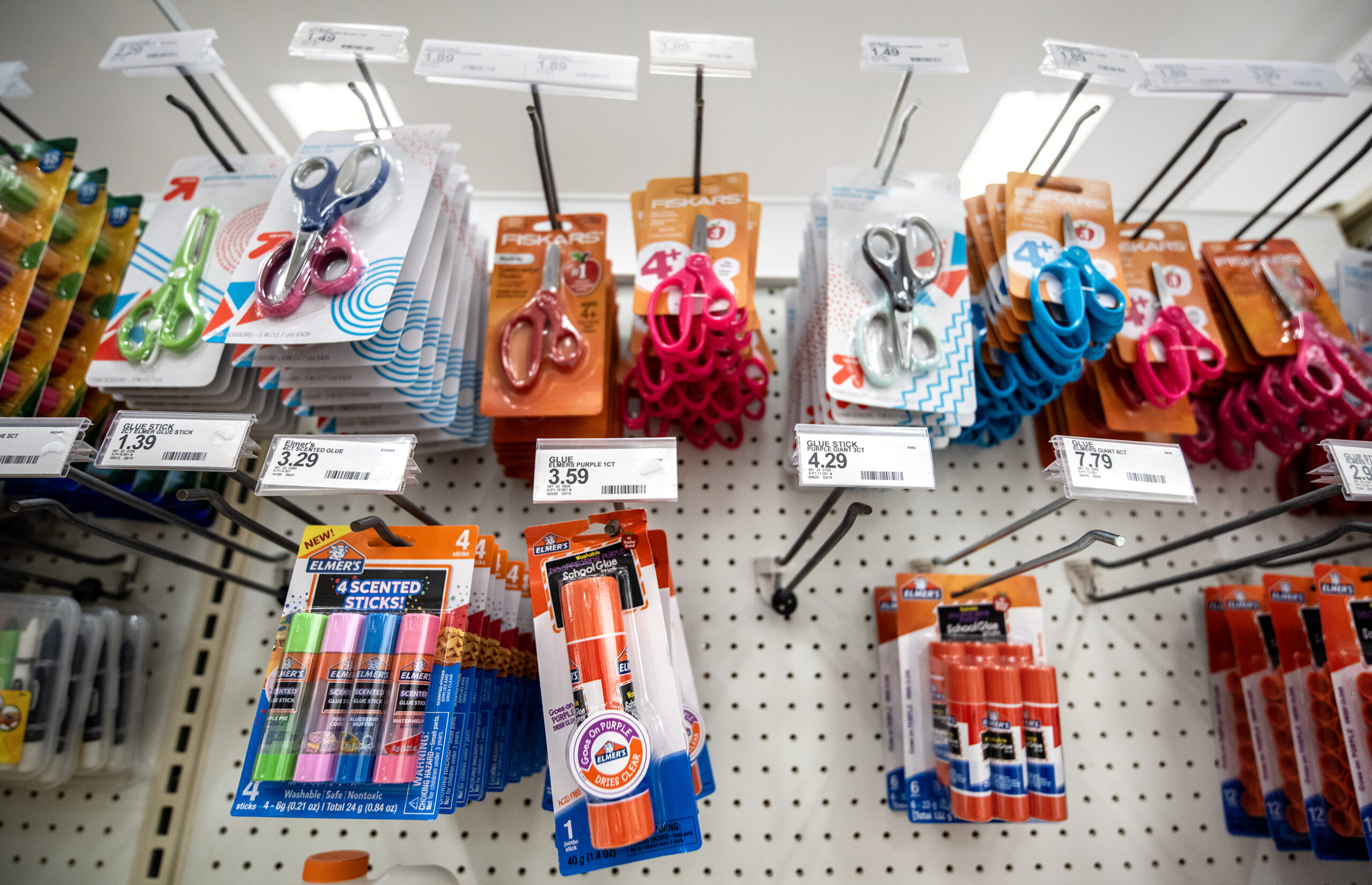 Glue sticks and scissors are displayed with prices on a shelf.