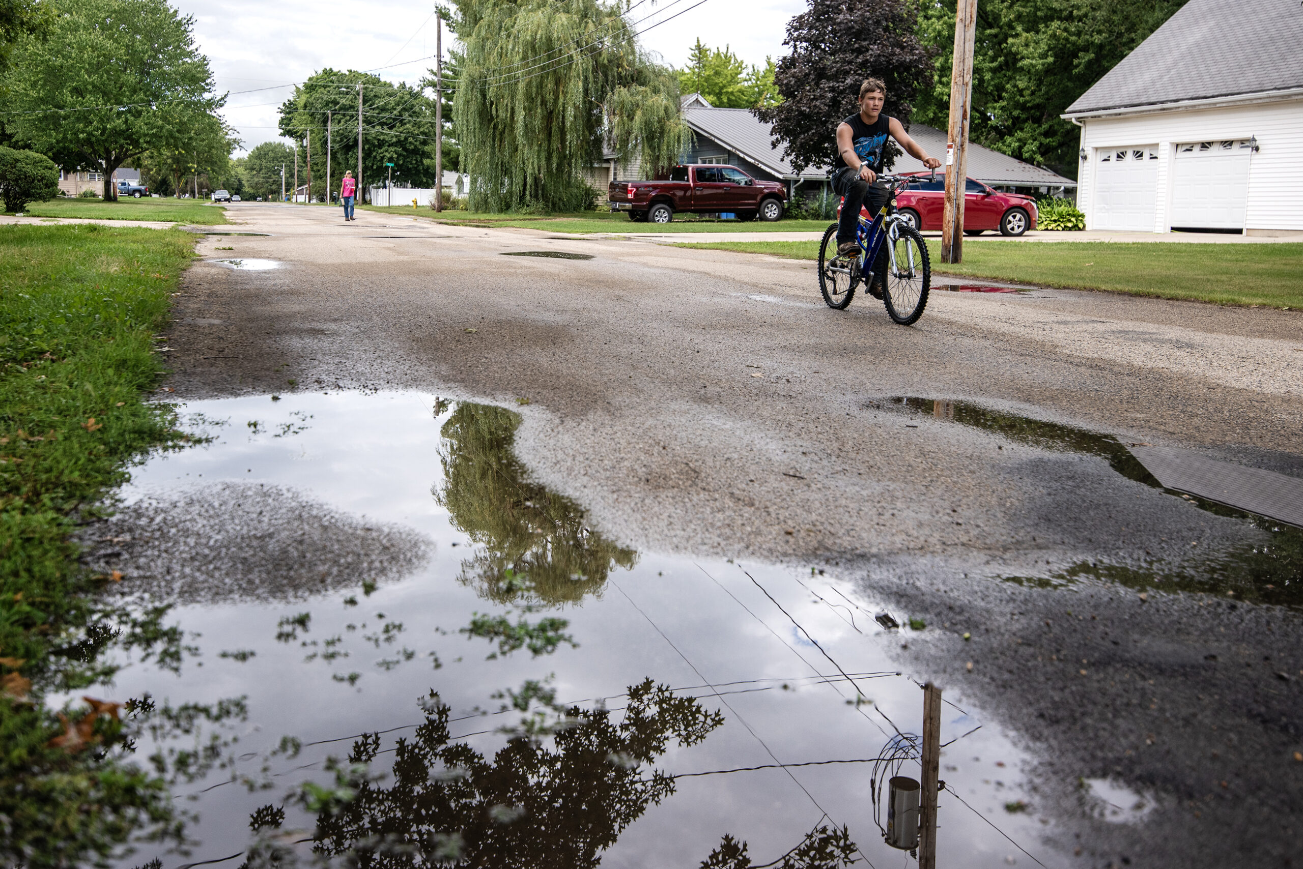 The reflection of trees can be seen in a puddle as a bicyclist passes by.