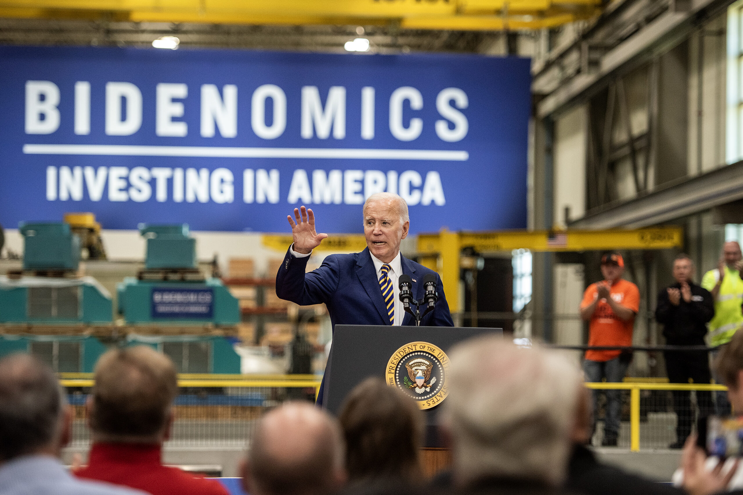 A large banner that says "Bidenomics" can be seen behind President Biden as he speaks from a stage.