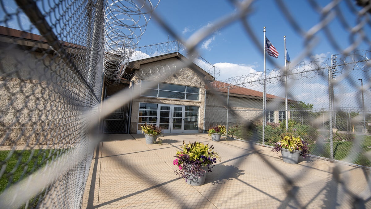 Four pots with flowers are displayed in front of the door to the correctional center. The entire area is surrounded by a barb wire fence.