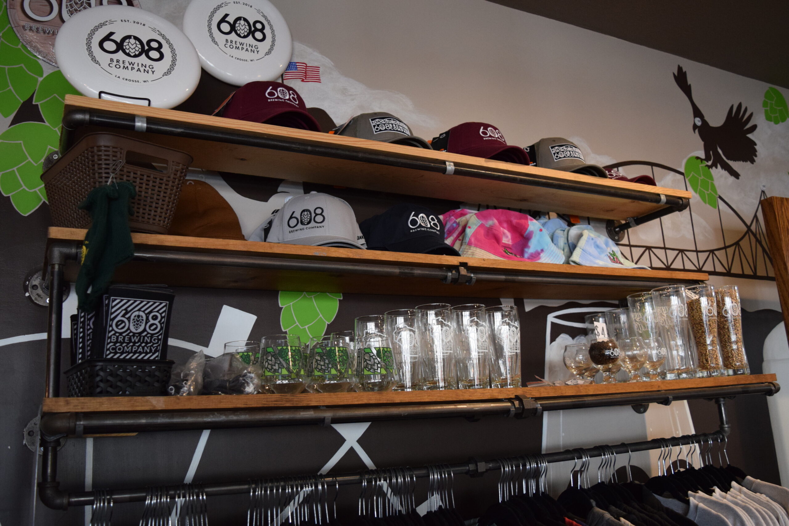 A shelf with baseball hats, beer glasses and koozies with the 608 Brewing Company logo