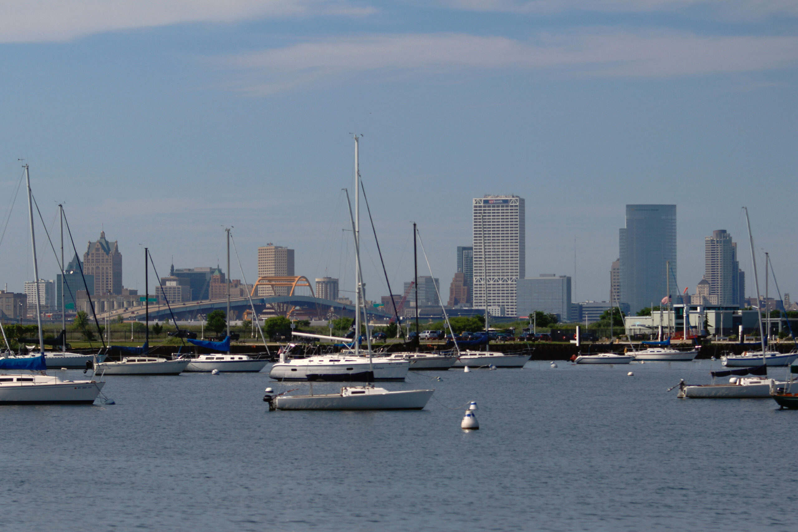 At least a dozen sailboats float off the shore of Milwaukee. The city's skyline is in the background.