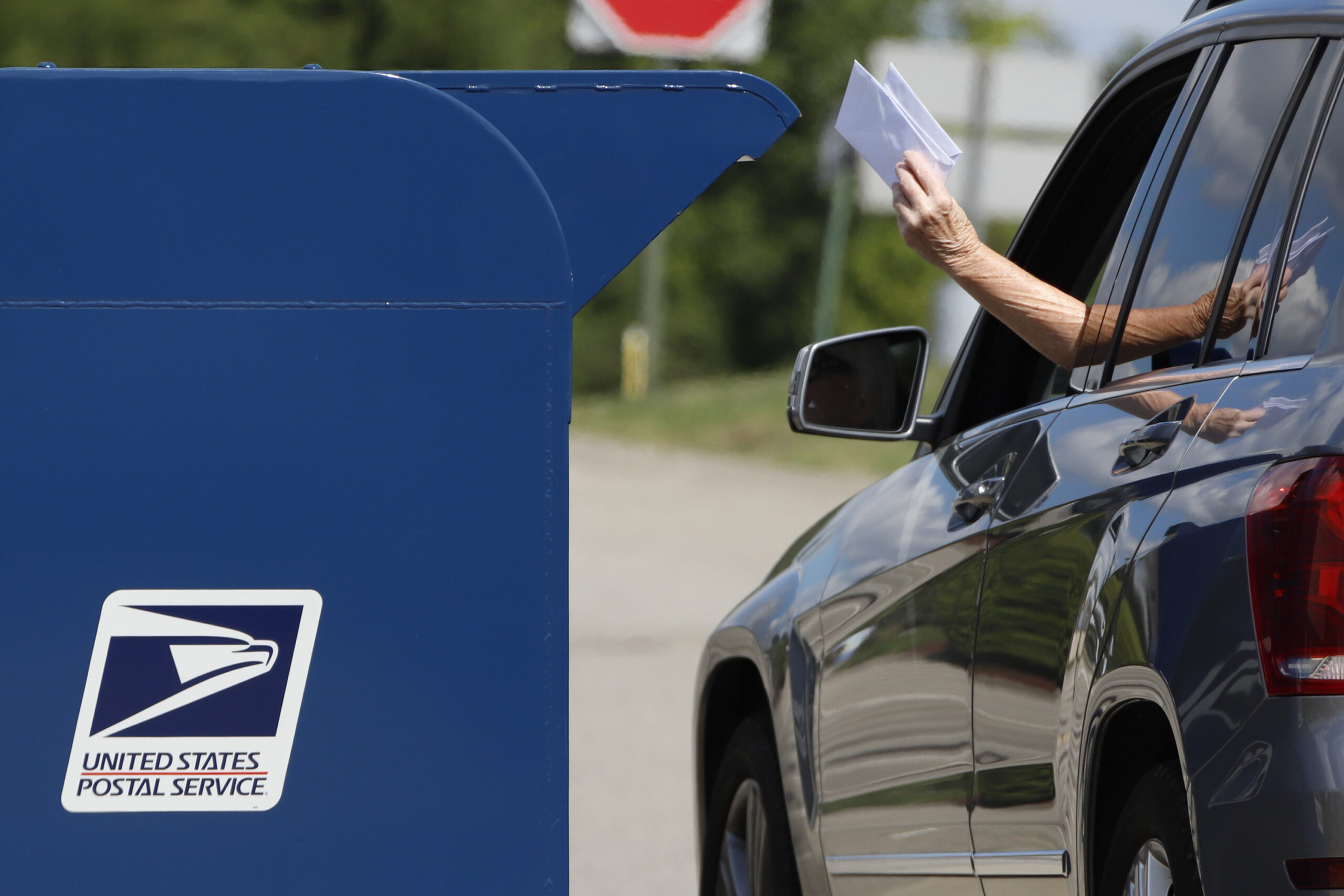 A person deposits mail in a USPS box